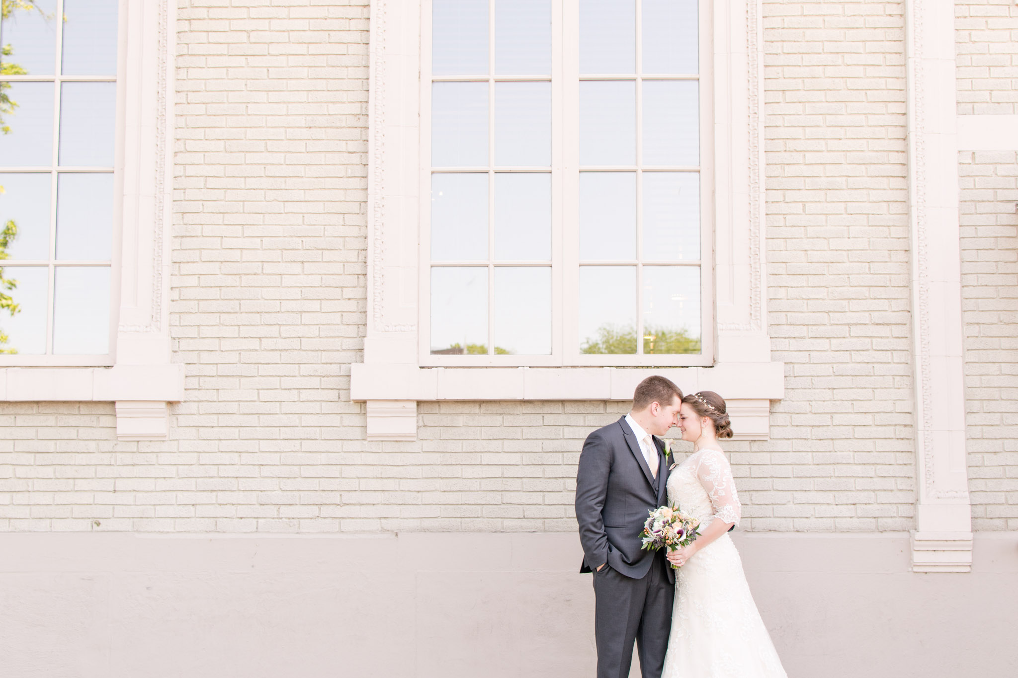 Bride and Groom softly smile in front of large window on wedding day