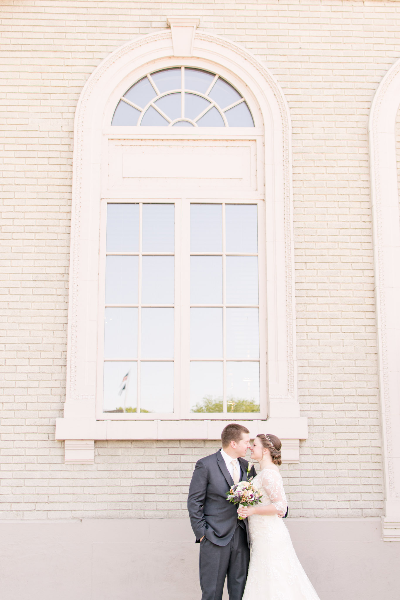 Bride and groom pose in front of large window