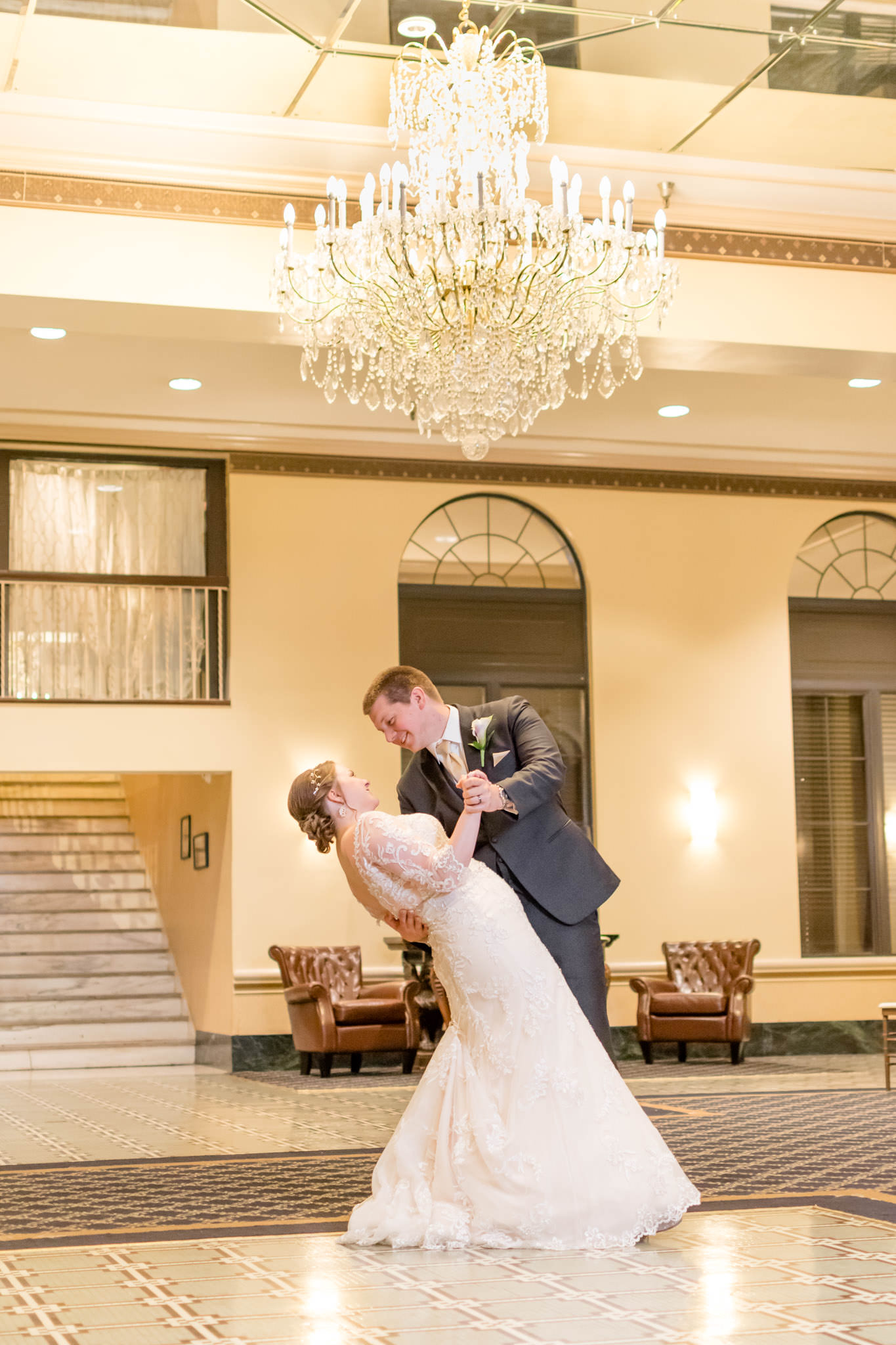 Groom dips bride under Marott chandelier