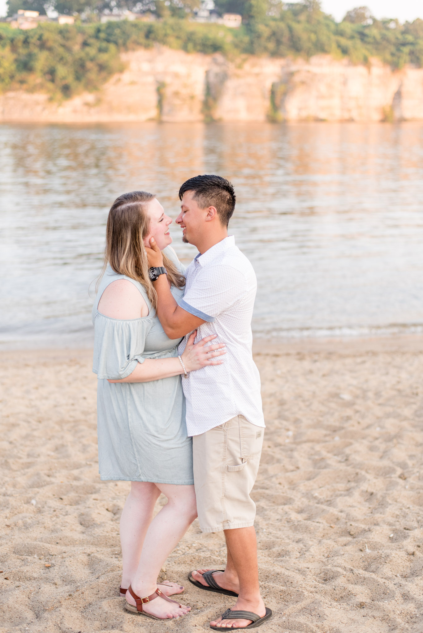 Couple laughs while kissing next to river for engagment pictures