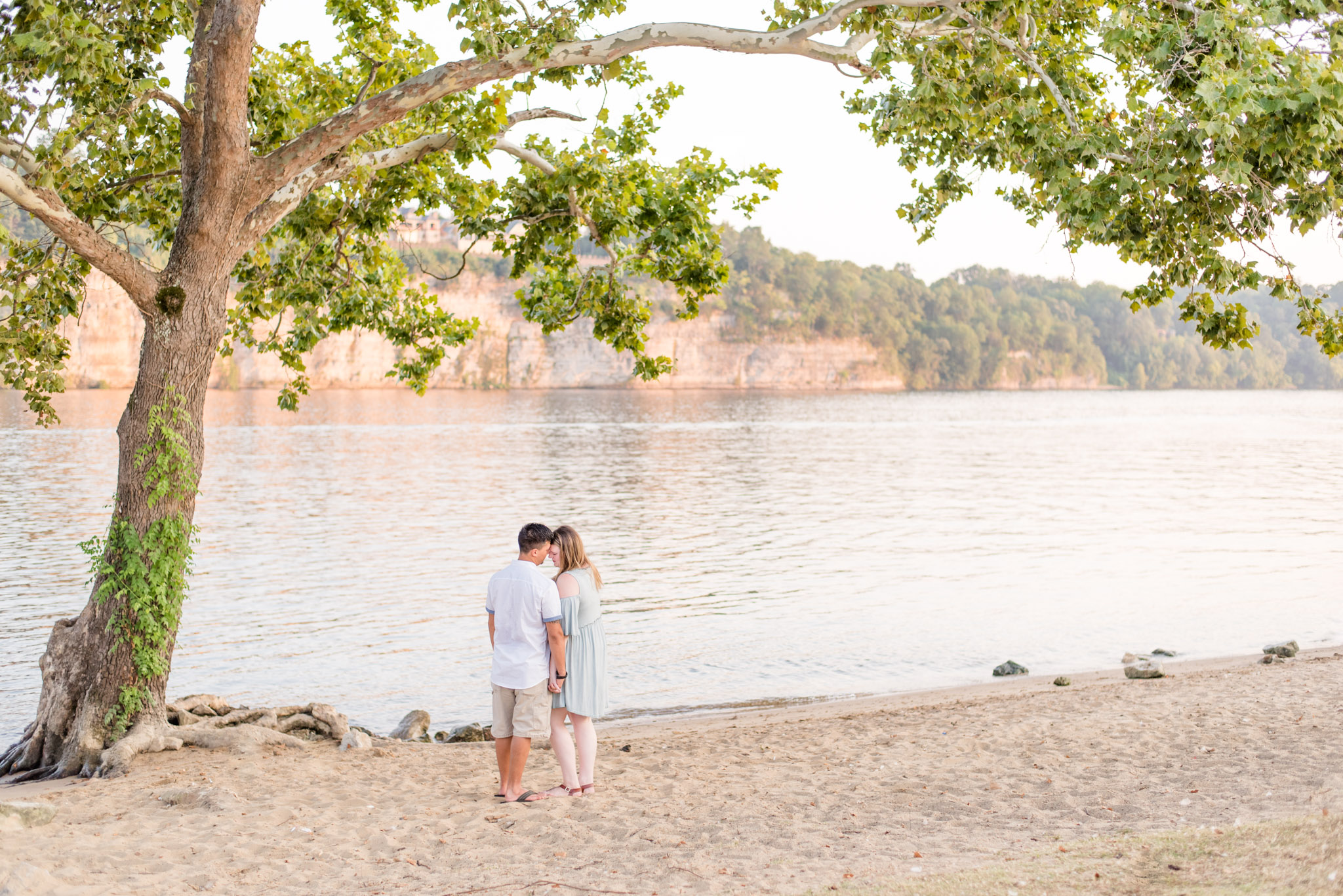 Couple snuggles under tree beside Alabama river during engagement pictures