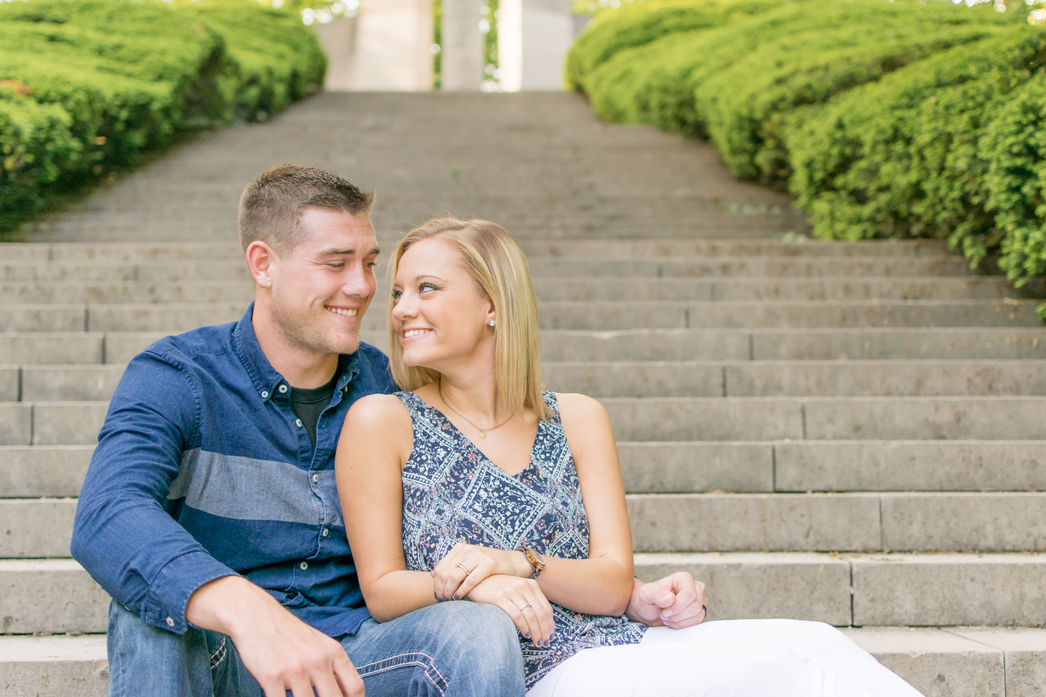 Couple smiles while sitting on stairs of Holcomb Gardens.