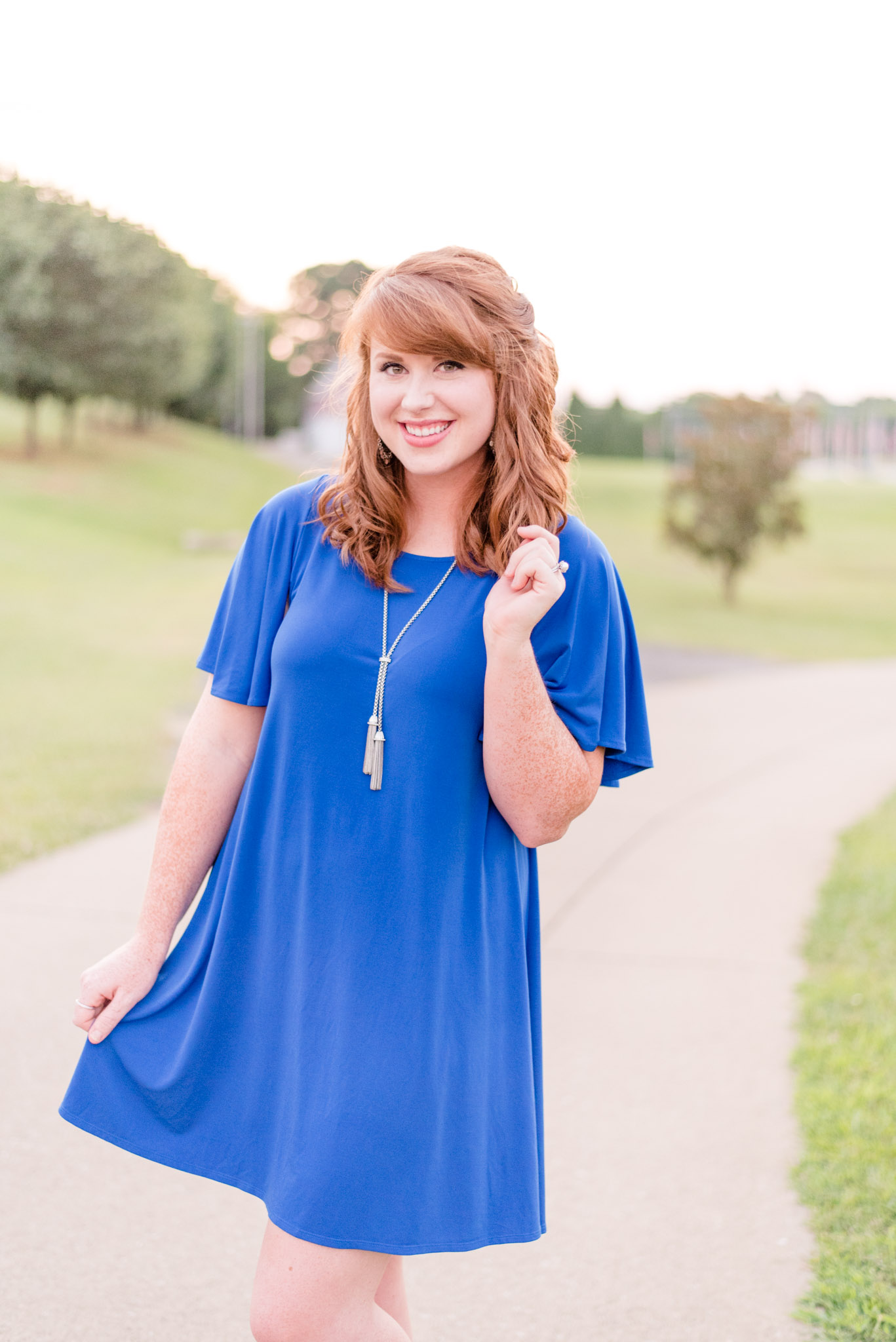 Red-headed model in blue dress smiles and poses for camera