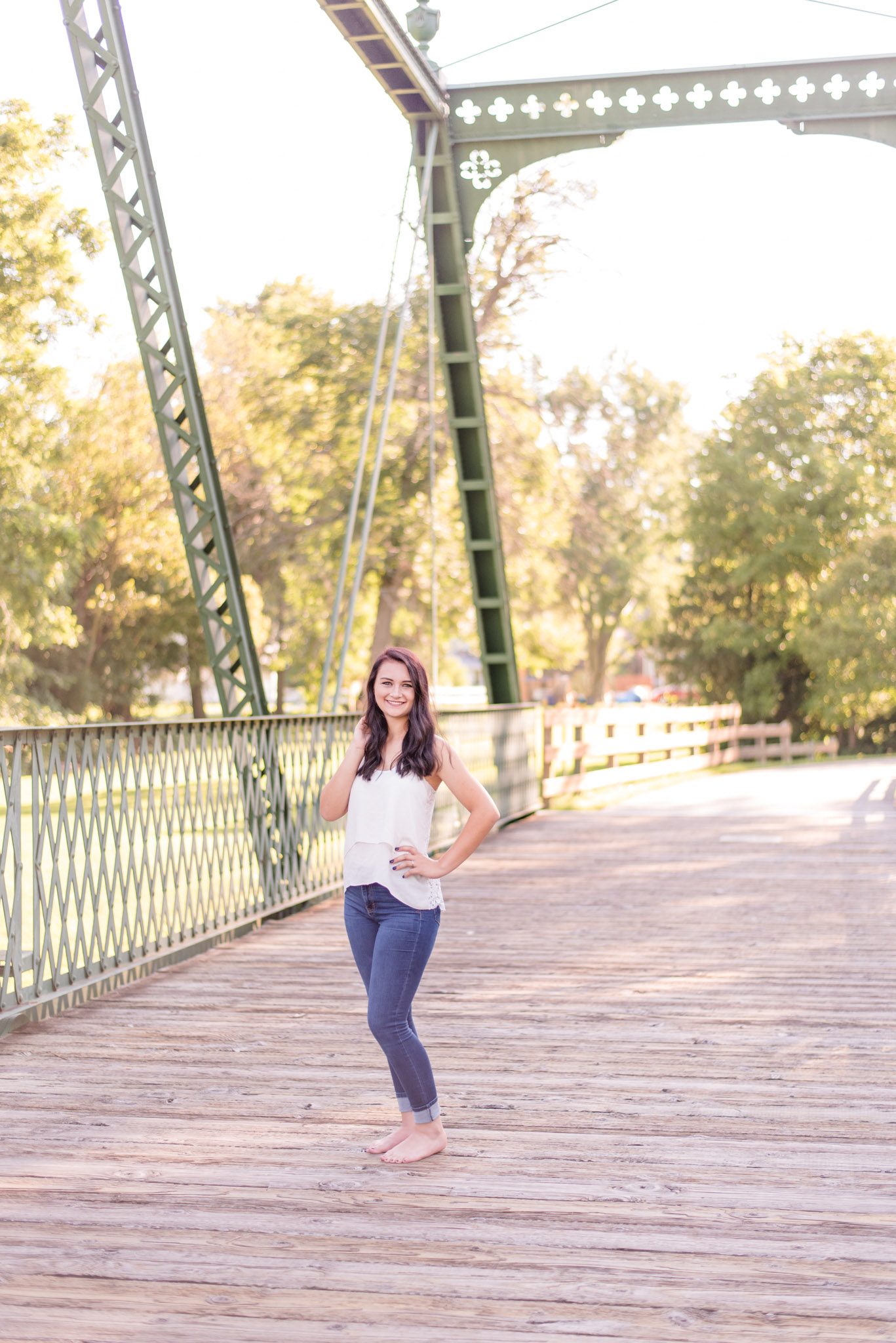 High school senior smiles and stands on bridge.