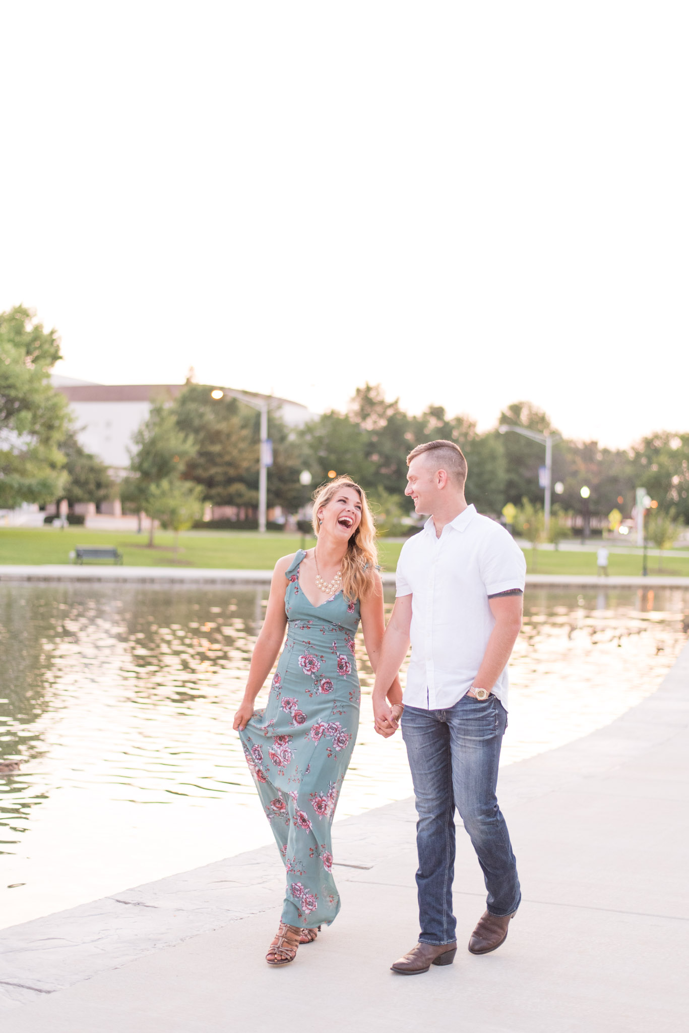 Engaged couple walks by lake and laughs.