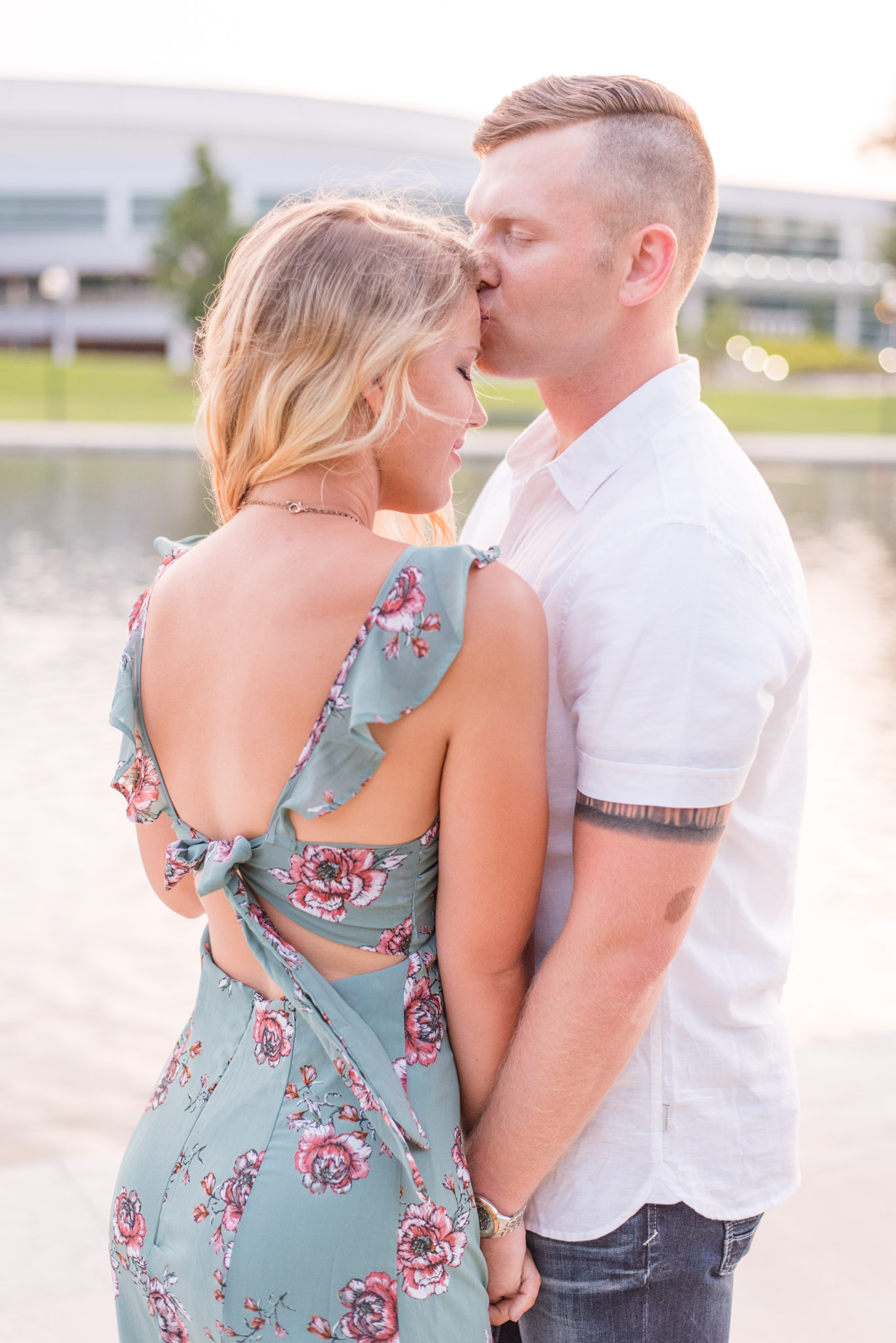 Groom kisses woman on forehead in front of lake. 