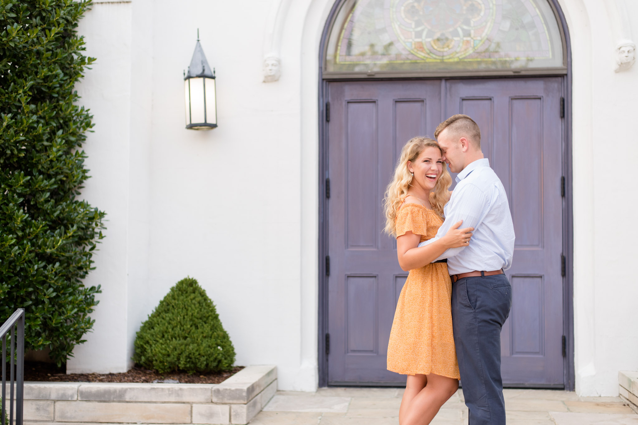 Engaged couple laughs in front of purple door.