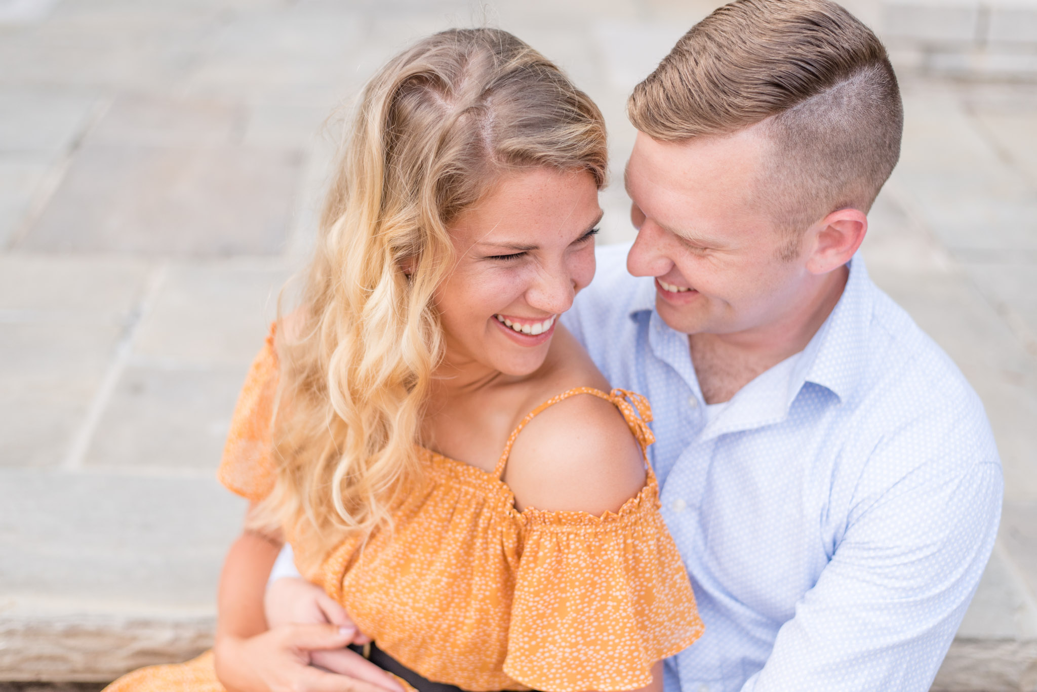 Engaged couple laughs while sitting on steps. 