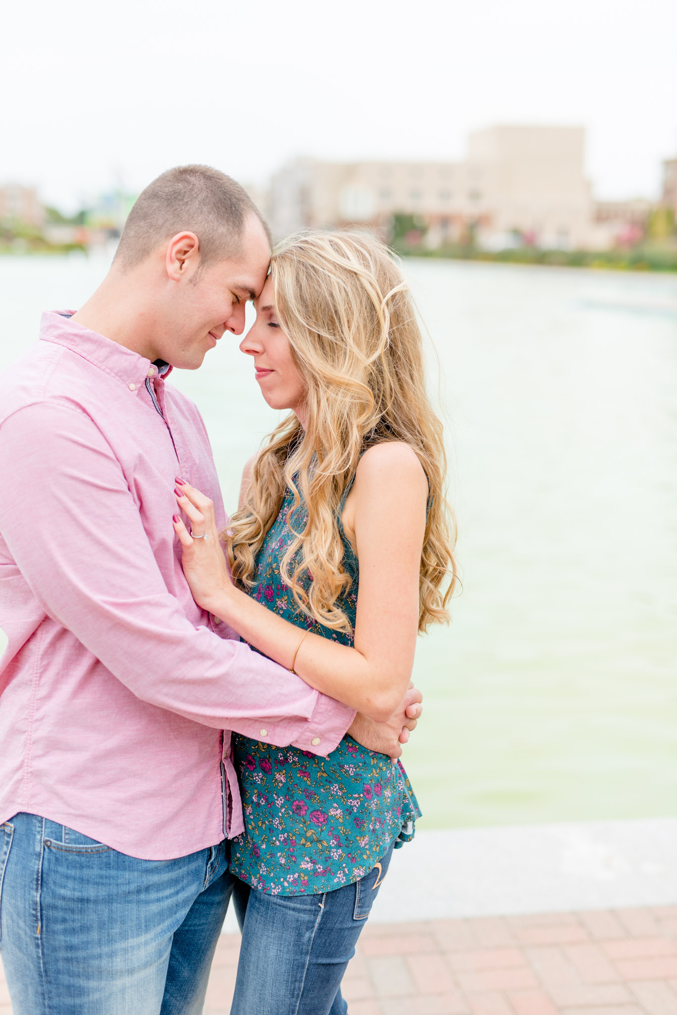 Engaged couple touch foreheads in front of reflecting pool.