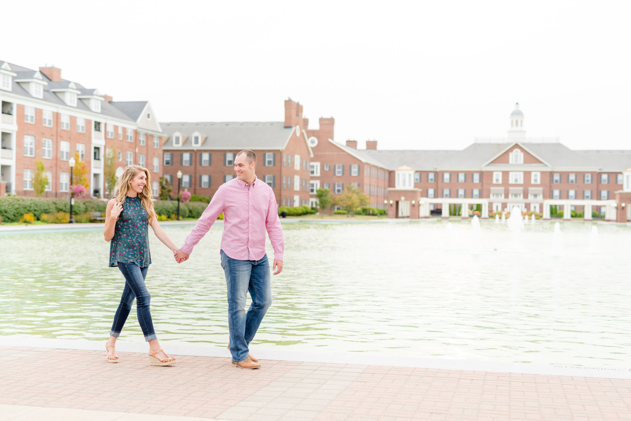 Engaged couple walk in front of large reflecting pool.