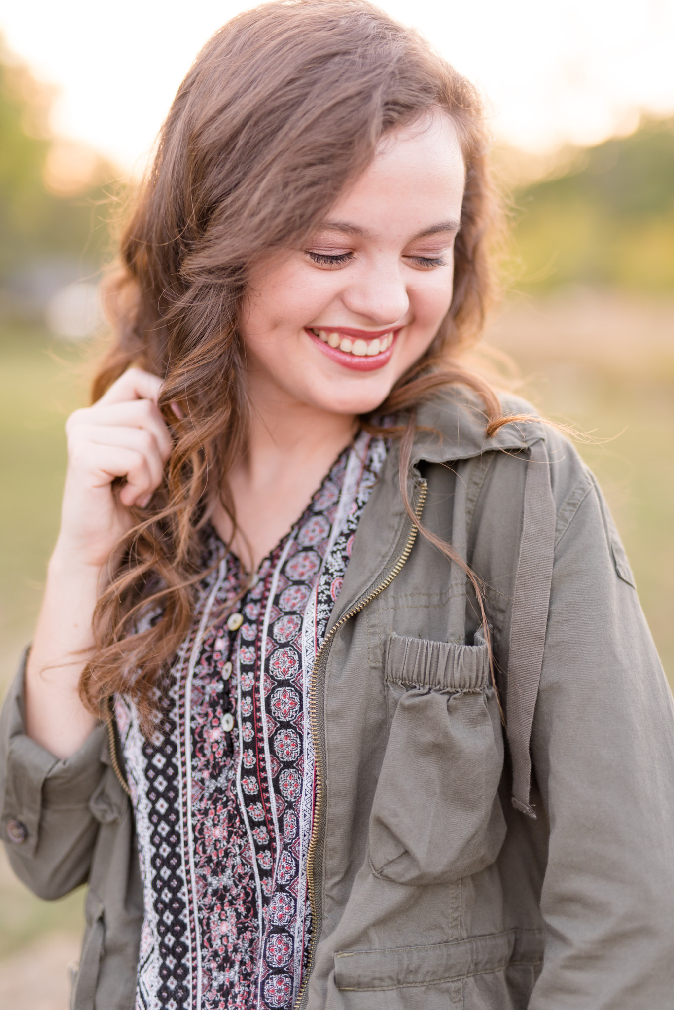 Senior girl laughs off camera in open field.