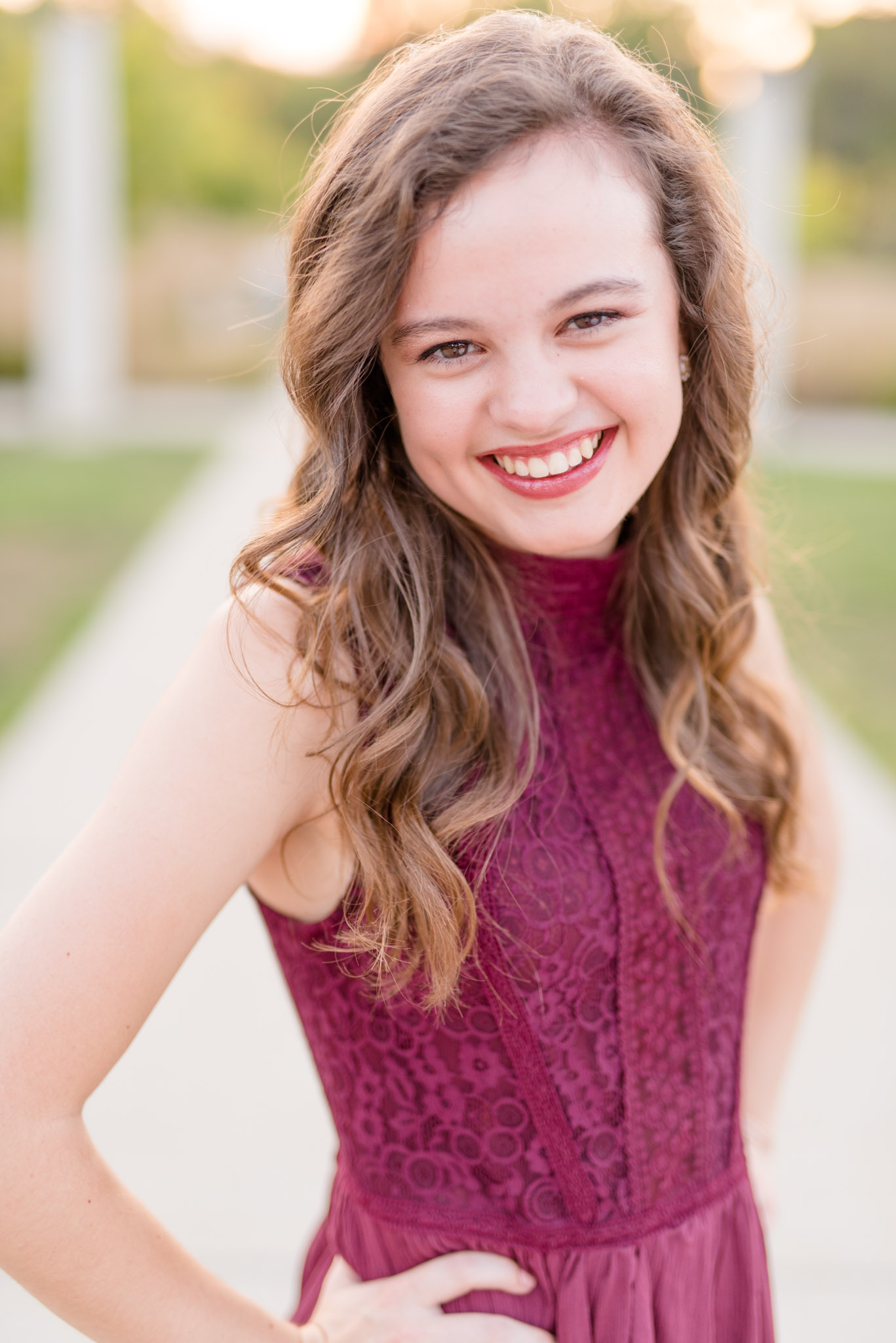 Senior girl smiles at camera with sunset in the background.