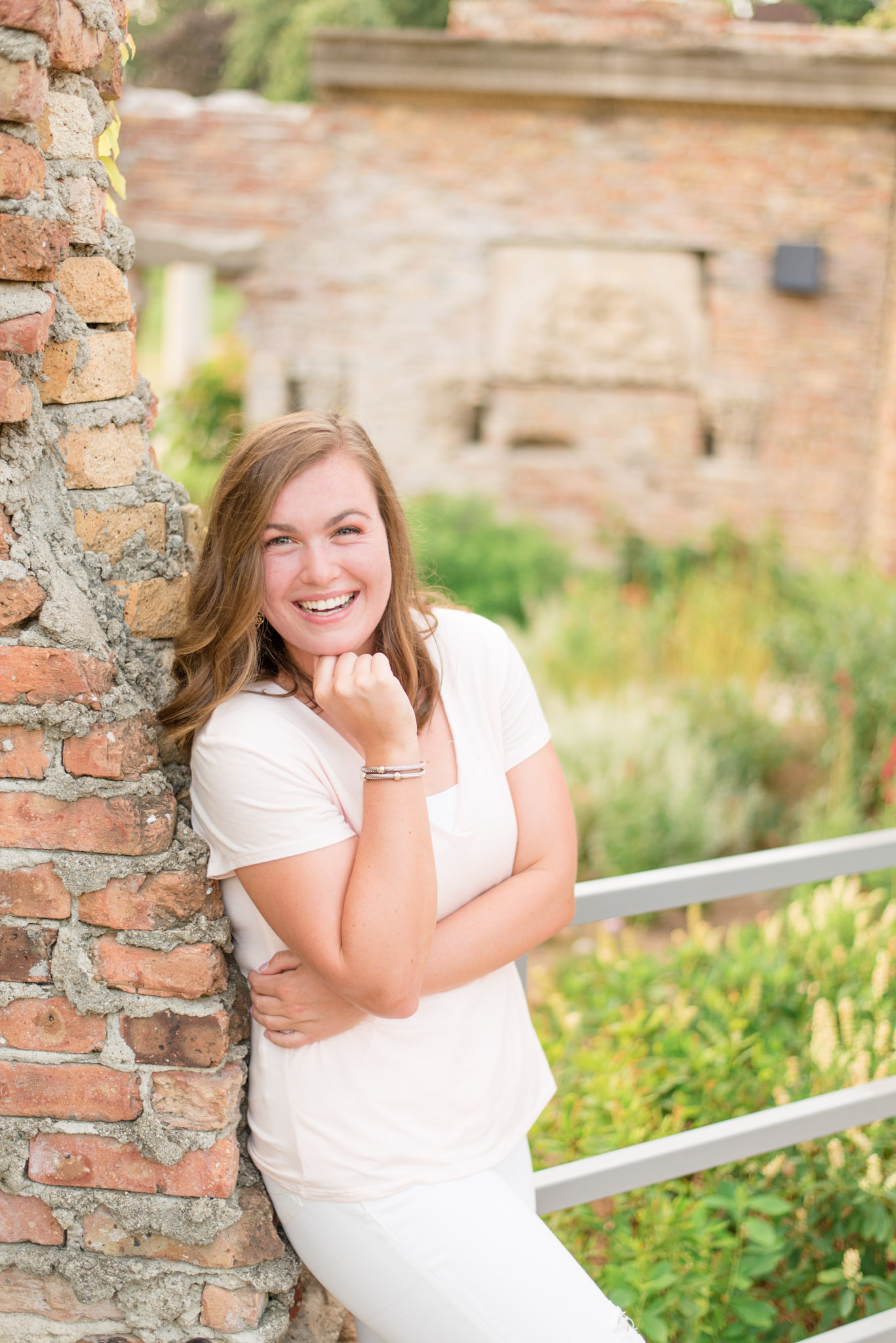 Senior leans against brick wall and laughs. 