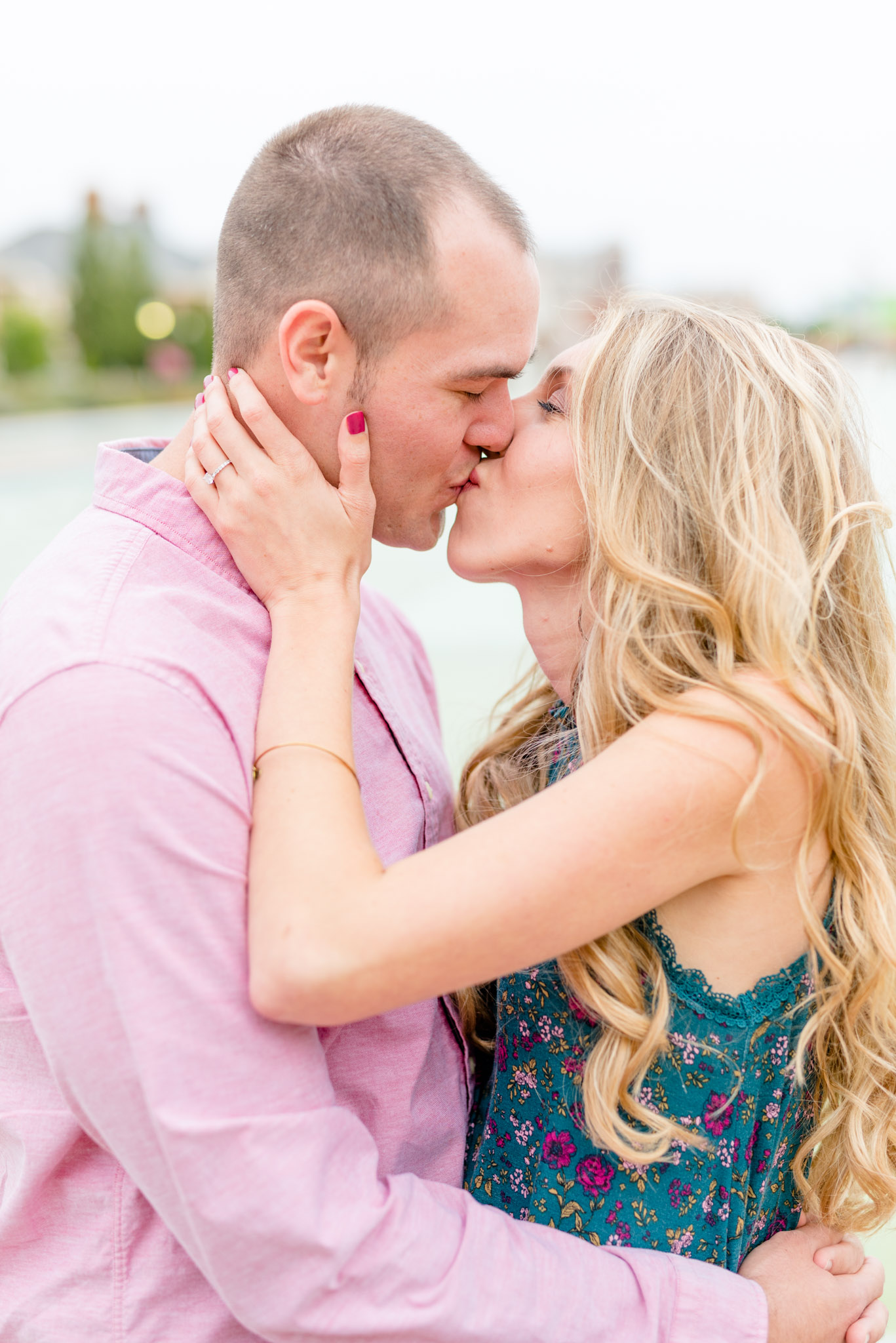 Engaged couple kisses in front of reflecting pool.
