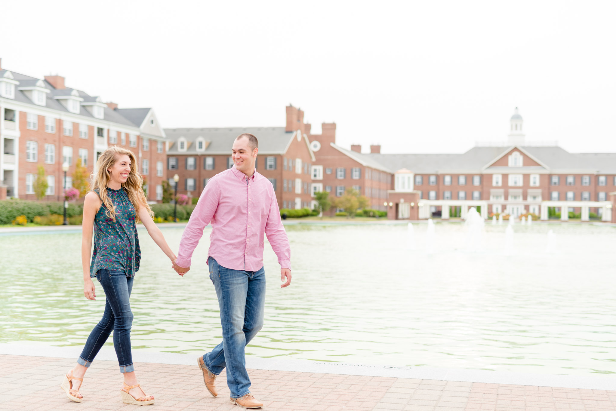 Engaged bride and groom walk in front of large building and water.