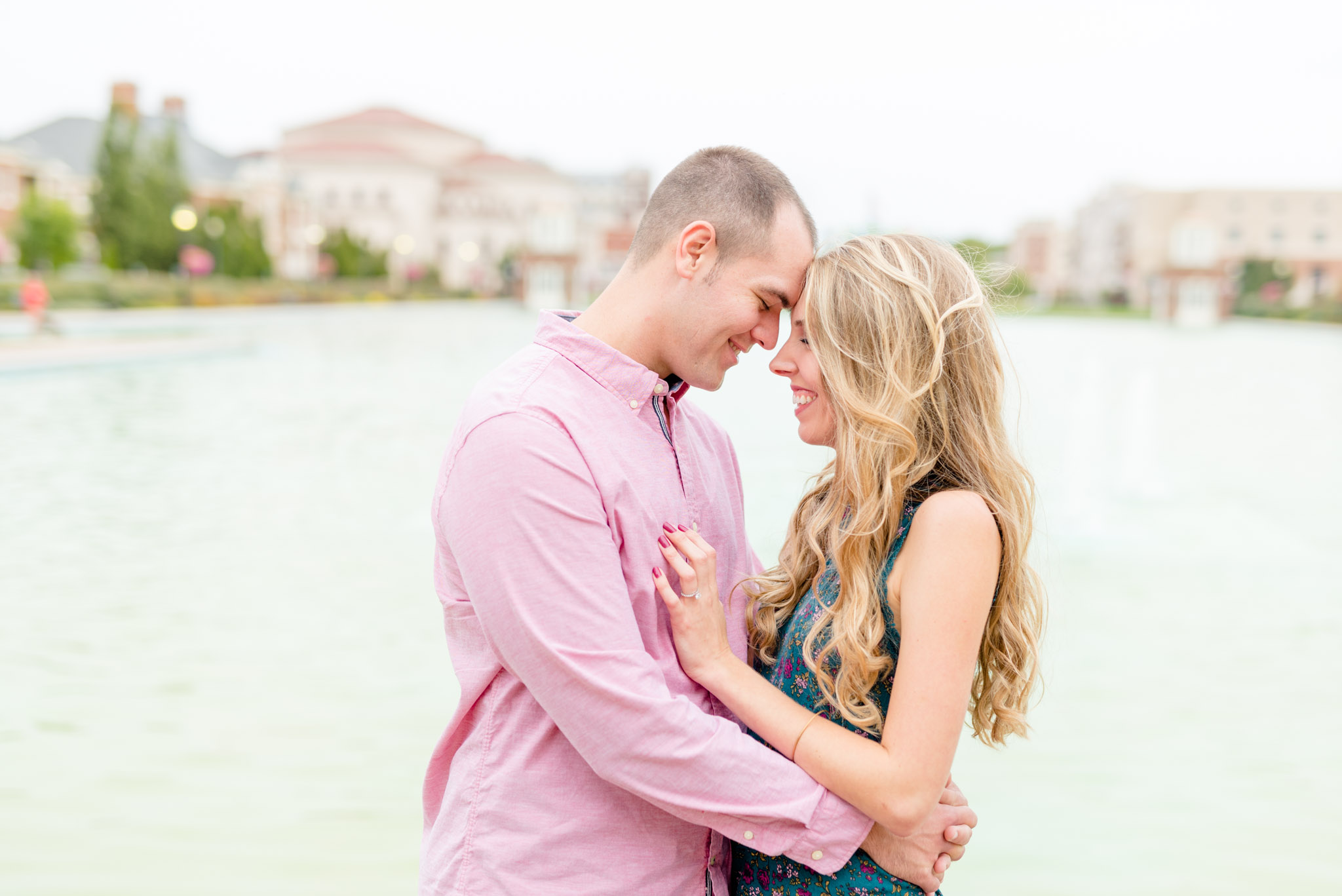 Bride and groom smiles as they hug in front of reflecting pool.