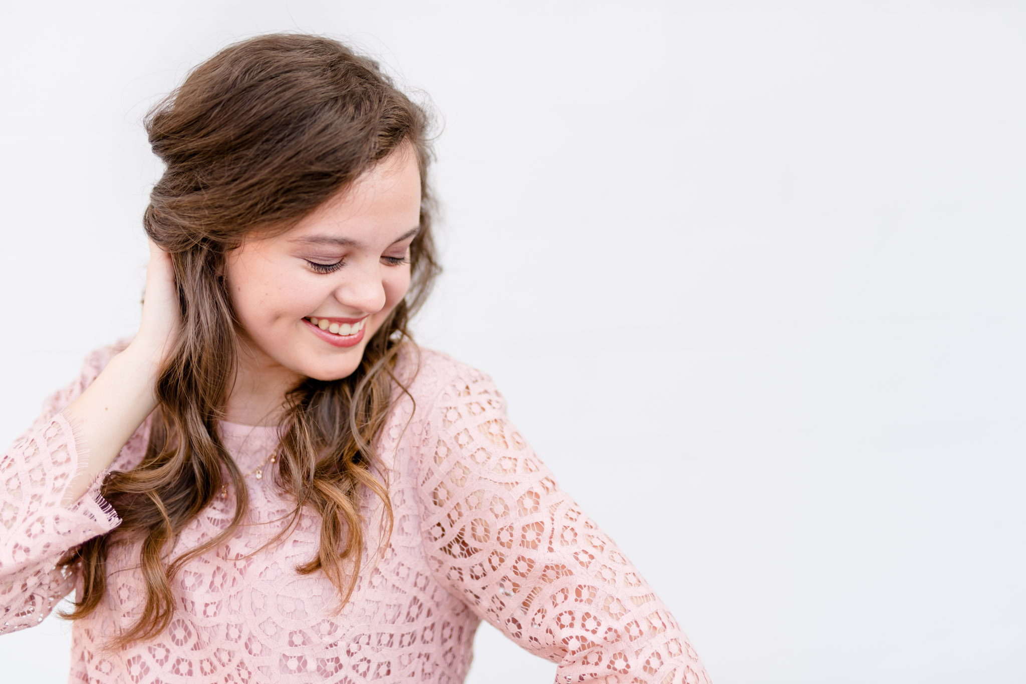 Senior girl smiles down shoulder with white background.