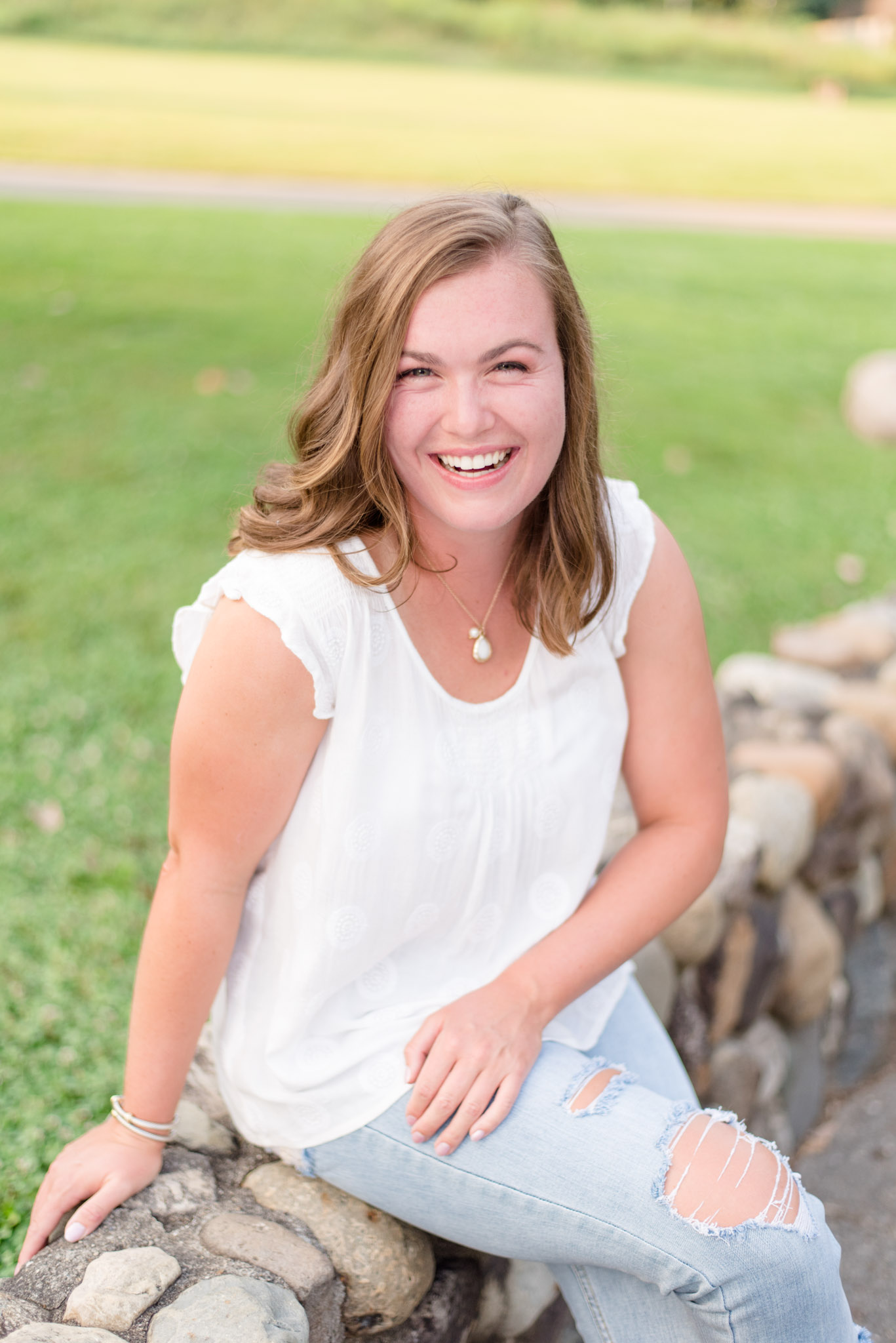 Senior laughs while sitting on stone wall. 