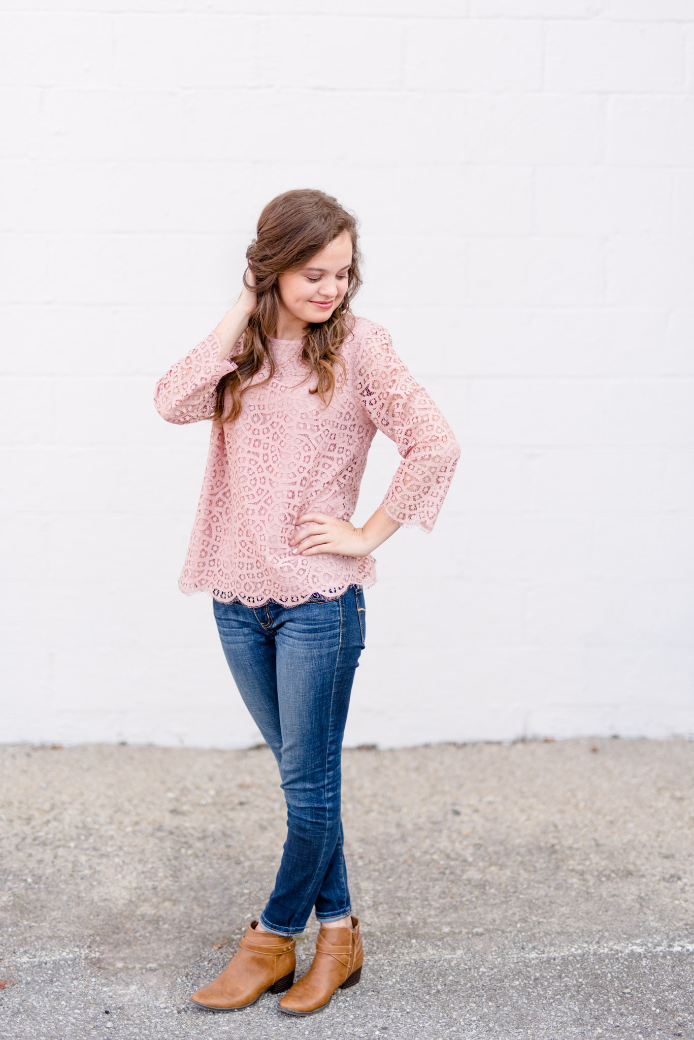 High School senior looks down shoulder in front of white wall.