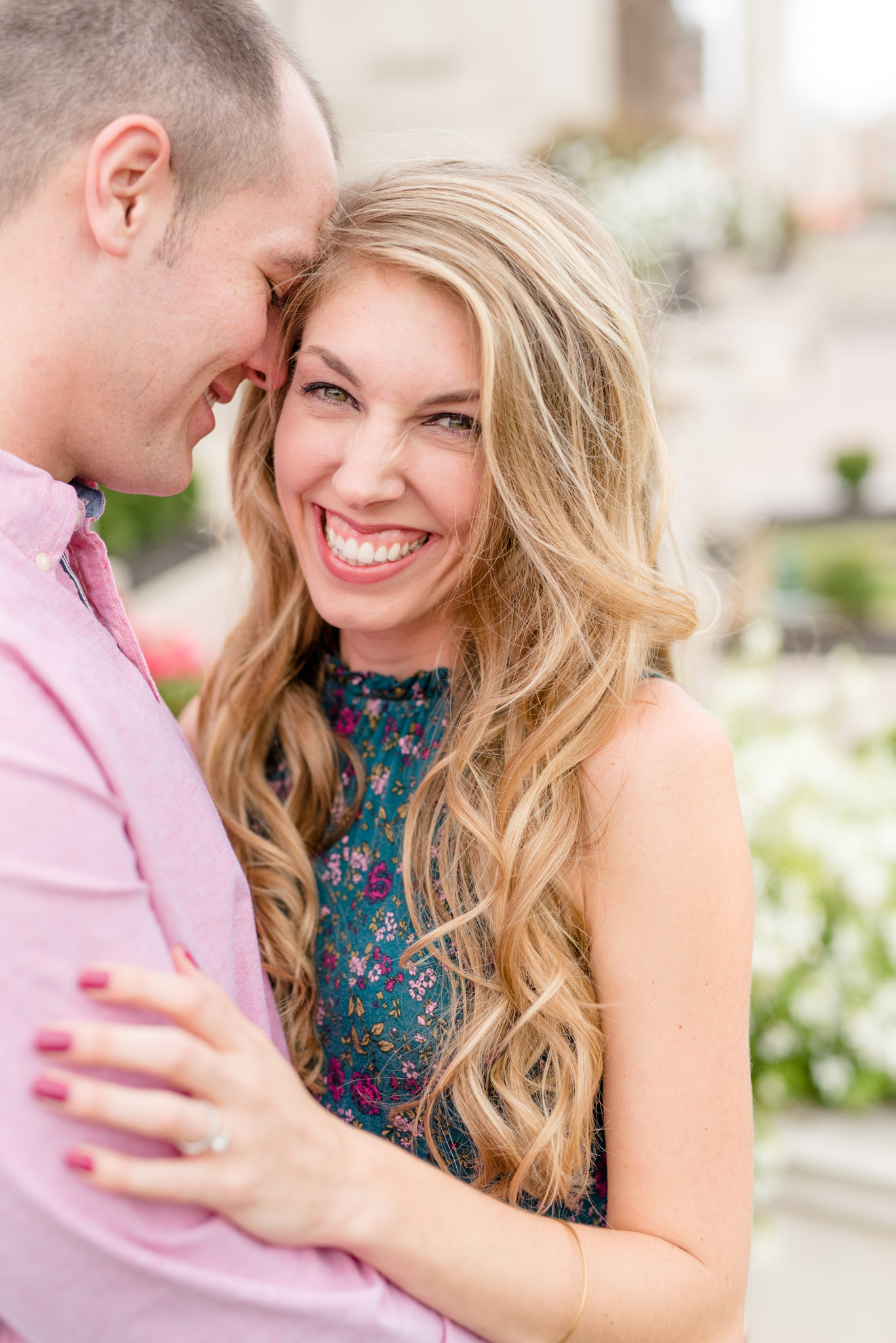 Engaged bride smiles at camera in front of white building.