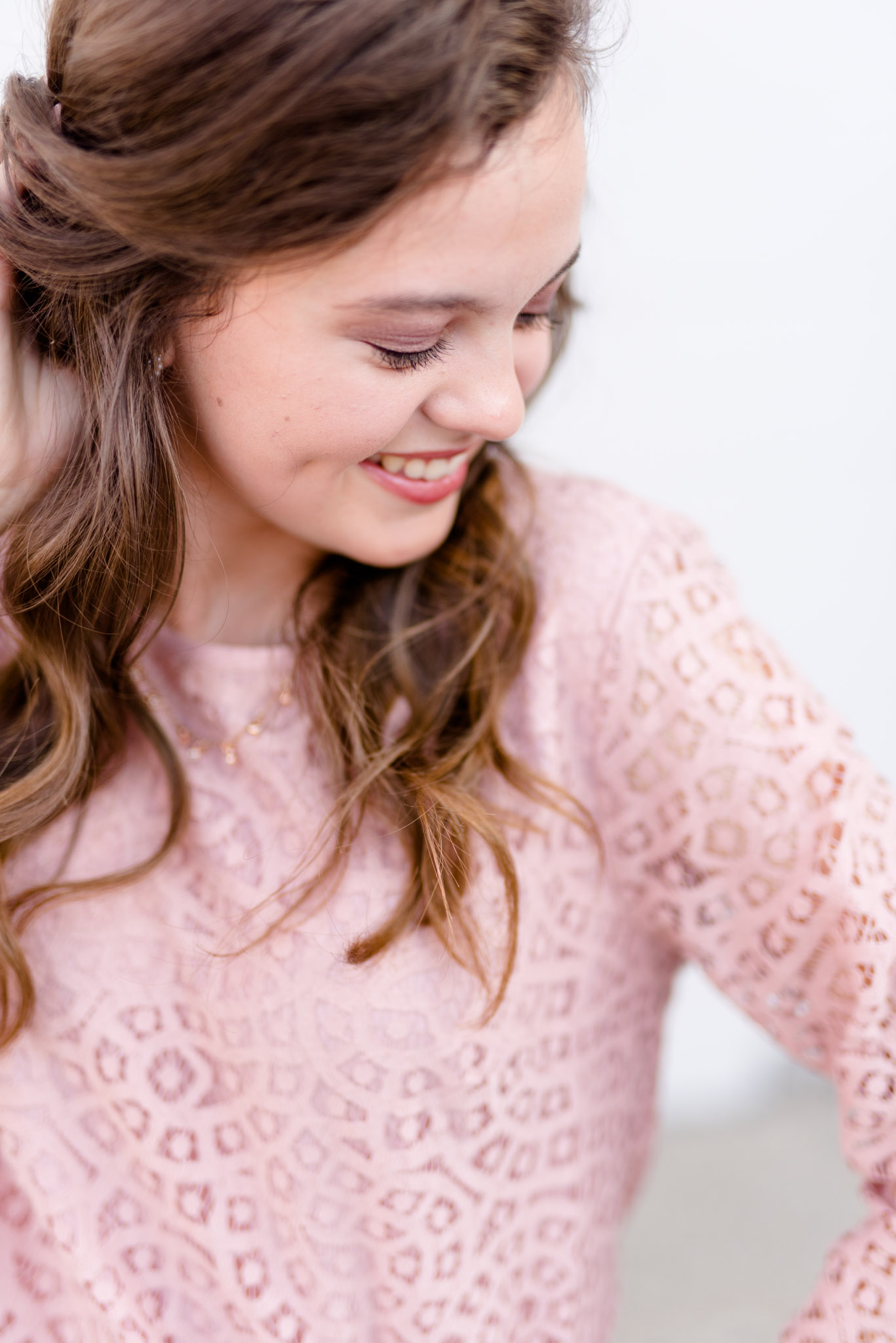 Senior girl looks down shoulder in front of white wall.