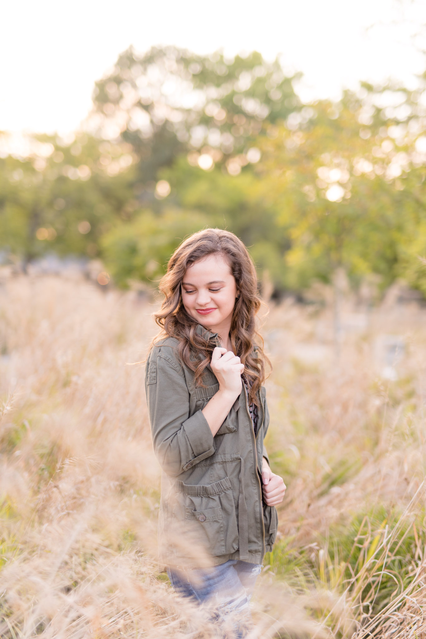 Senior girls looks down shoulder in field of tall grass.