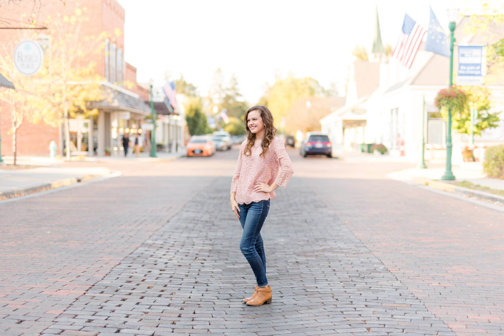 High school senior stands on brick road and smiles off camera.