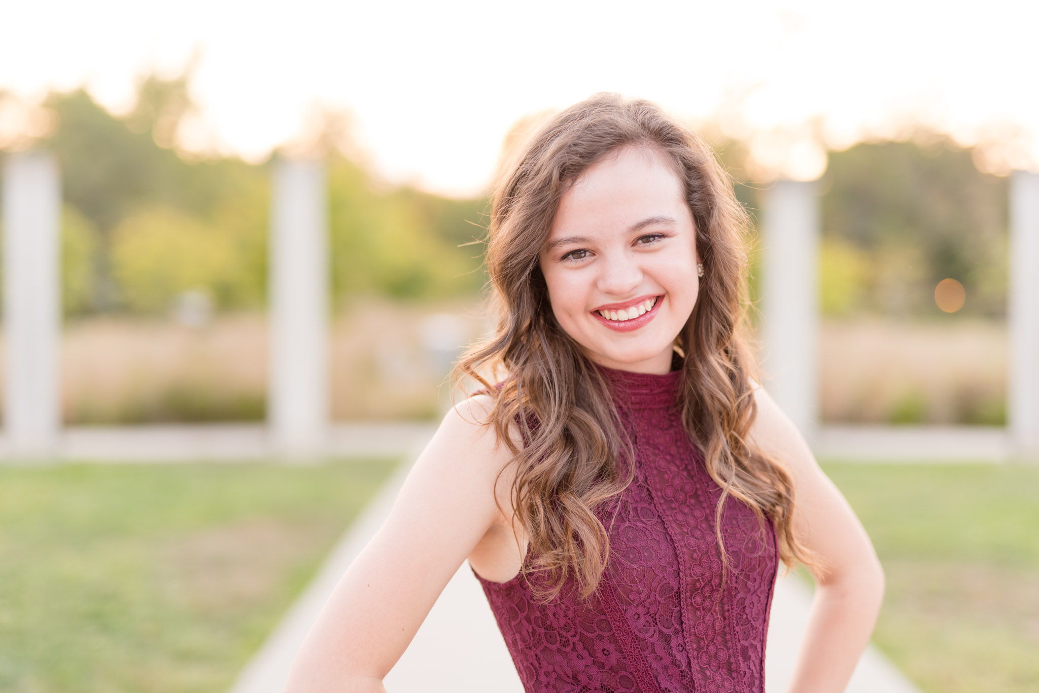 Senior girl smiles at the camera with hands on hips.