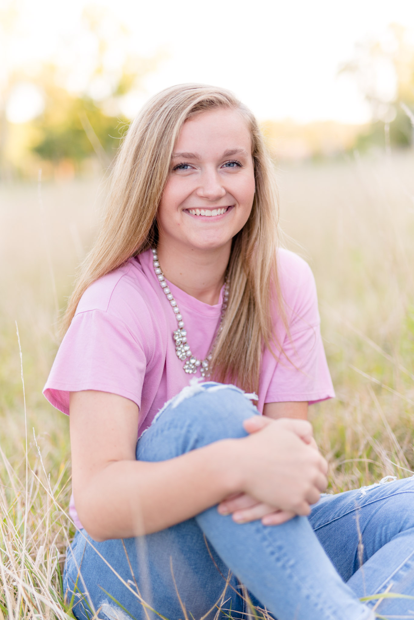 High School Senior sits in field and smiles for pictures