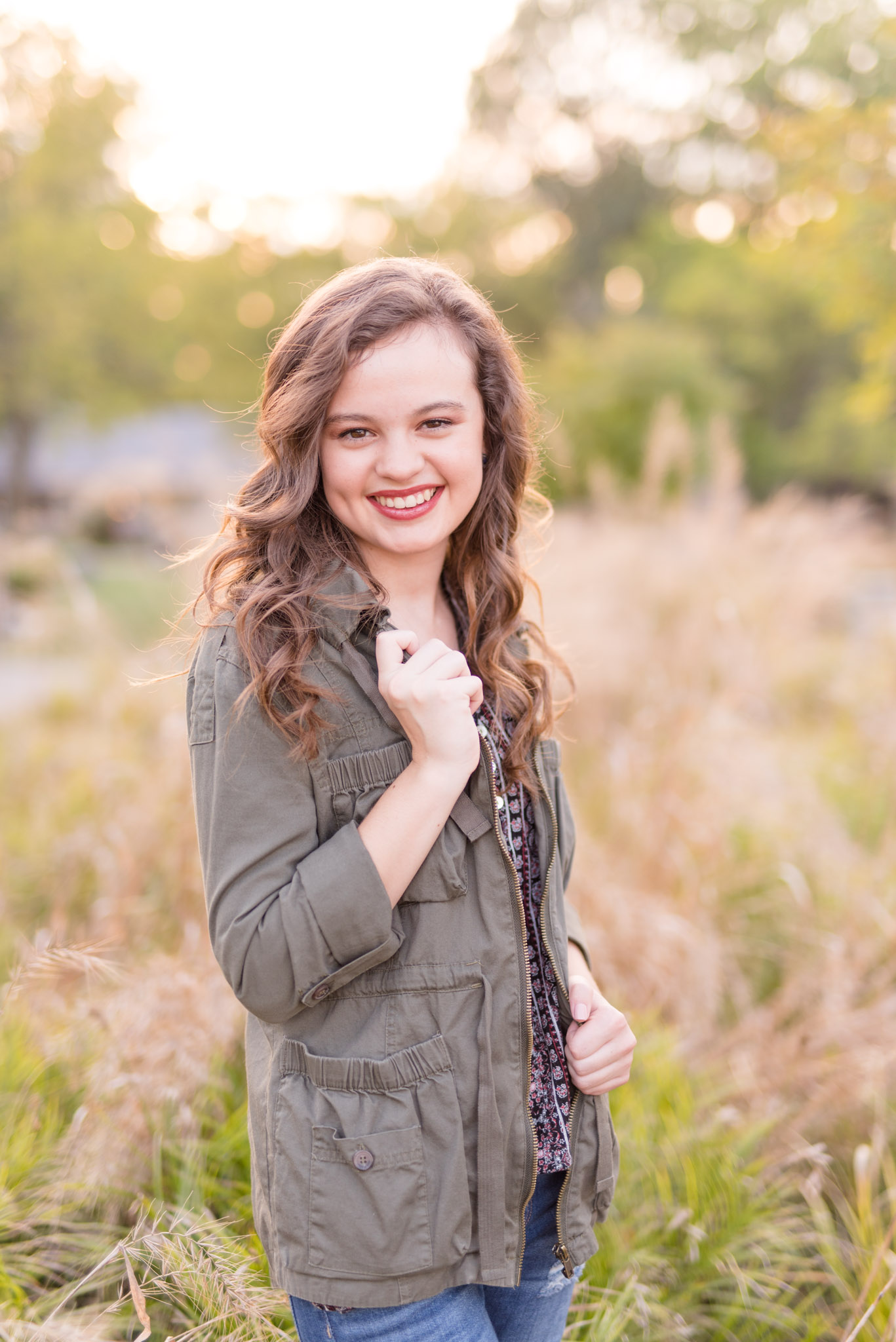 High school senior stands in tall grass and smiles.