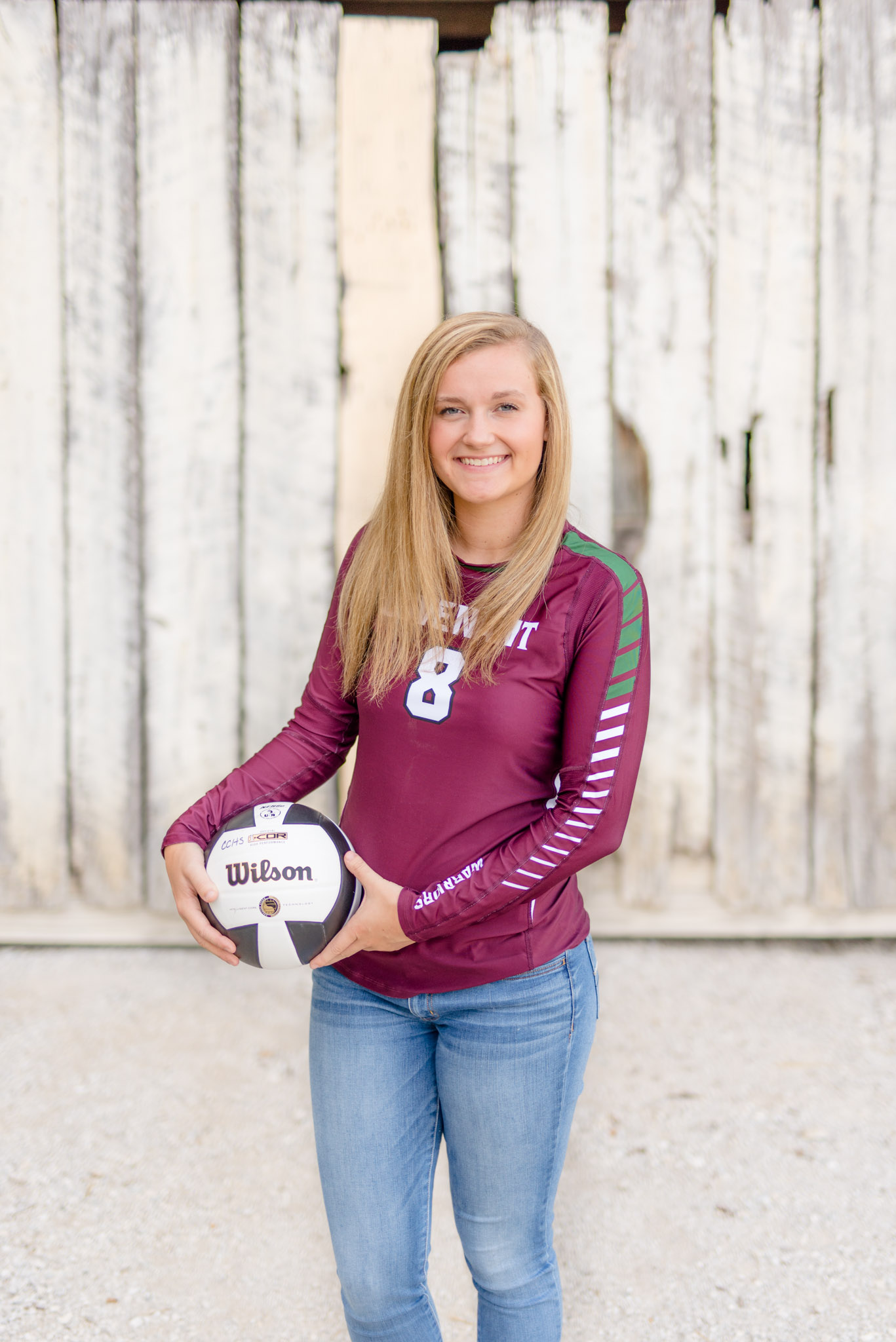 Senior girl smiles while holding volleyball to the side.