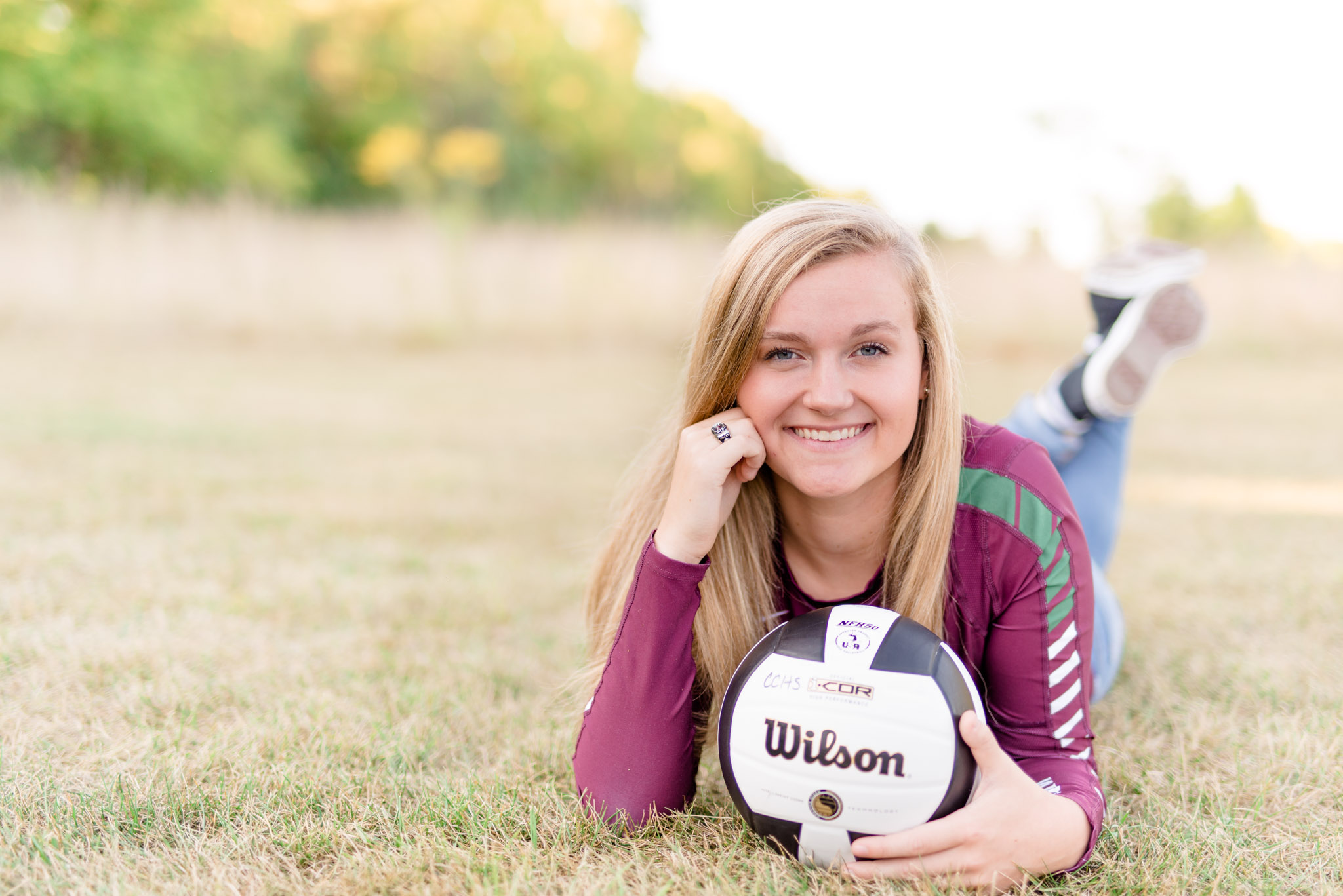 Senior girl holds volleyball in field and smiles.