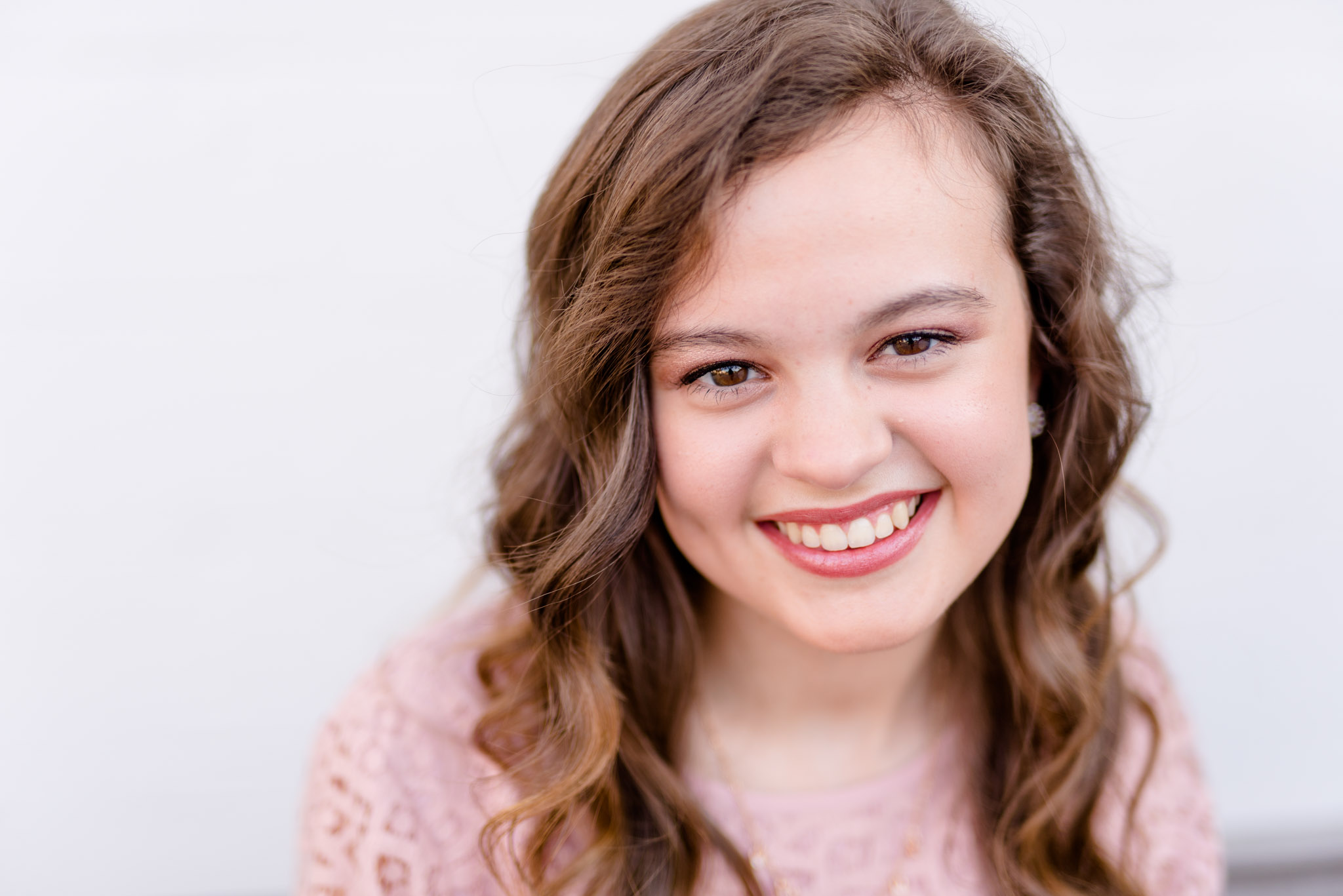 Senior girl headshot with white wall in background.