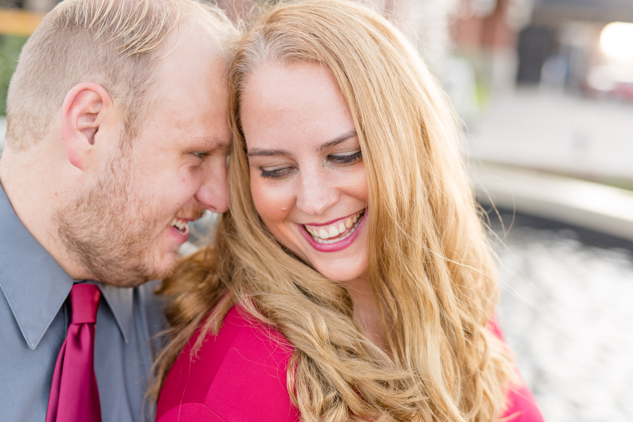 Man and woman laugh while sitting on fountain.