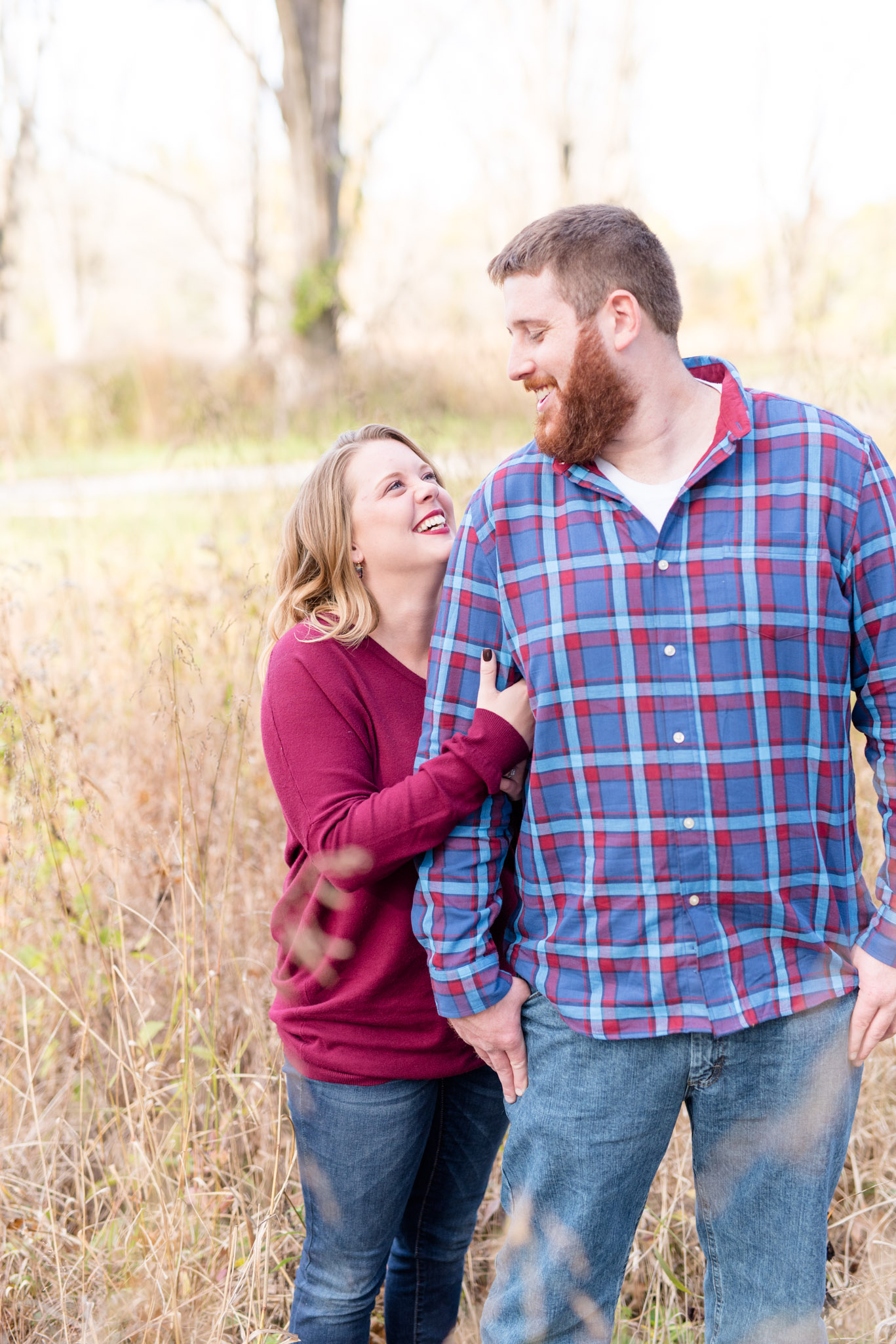 Couple looks at each other and laughs in fall field.