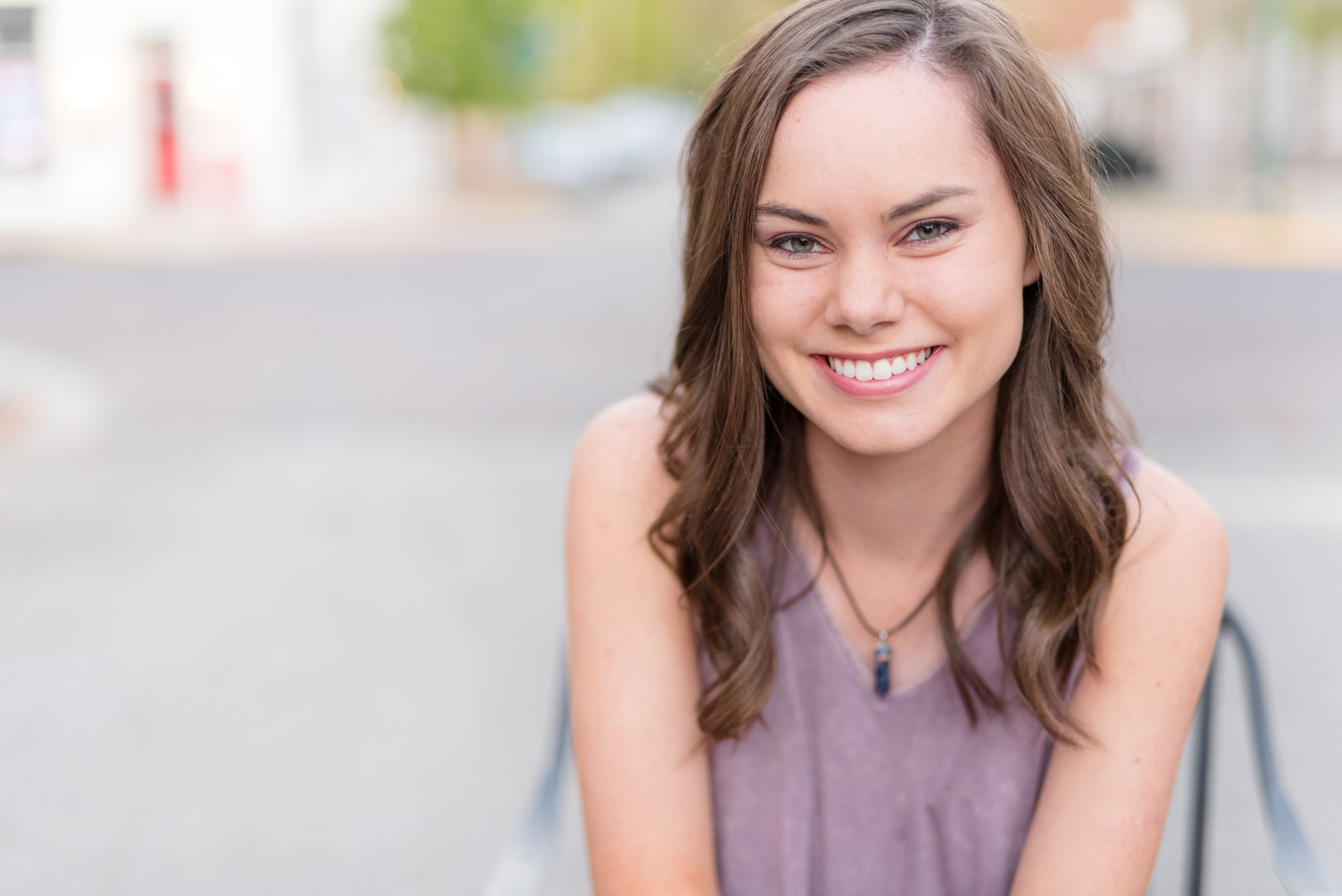 Senior girl smiles while sitting in chair downtown.