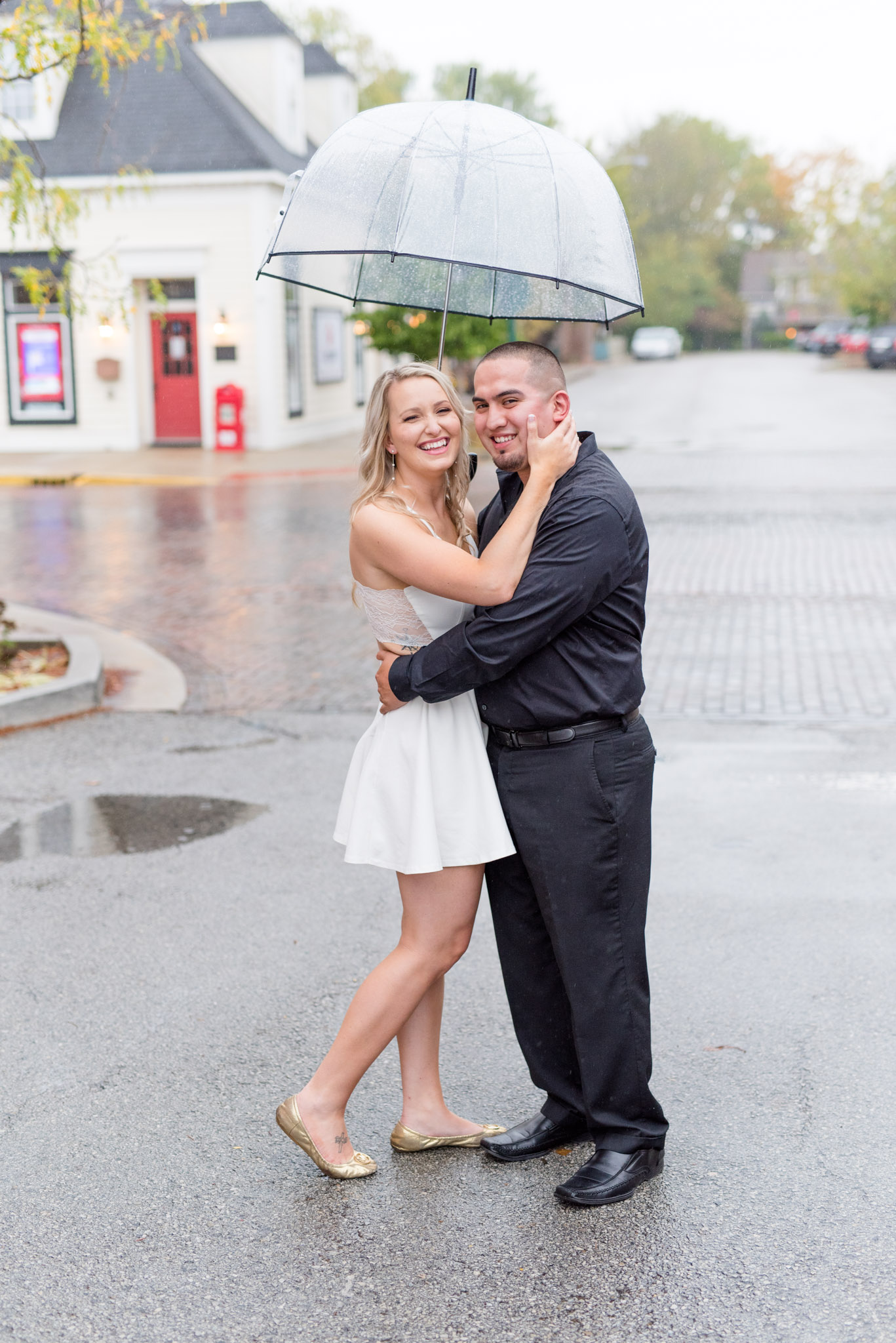 Bride and groom laugh under umbrella.