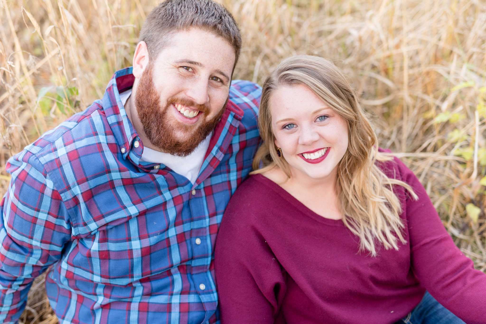 Couple smiles while sitting in field.