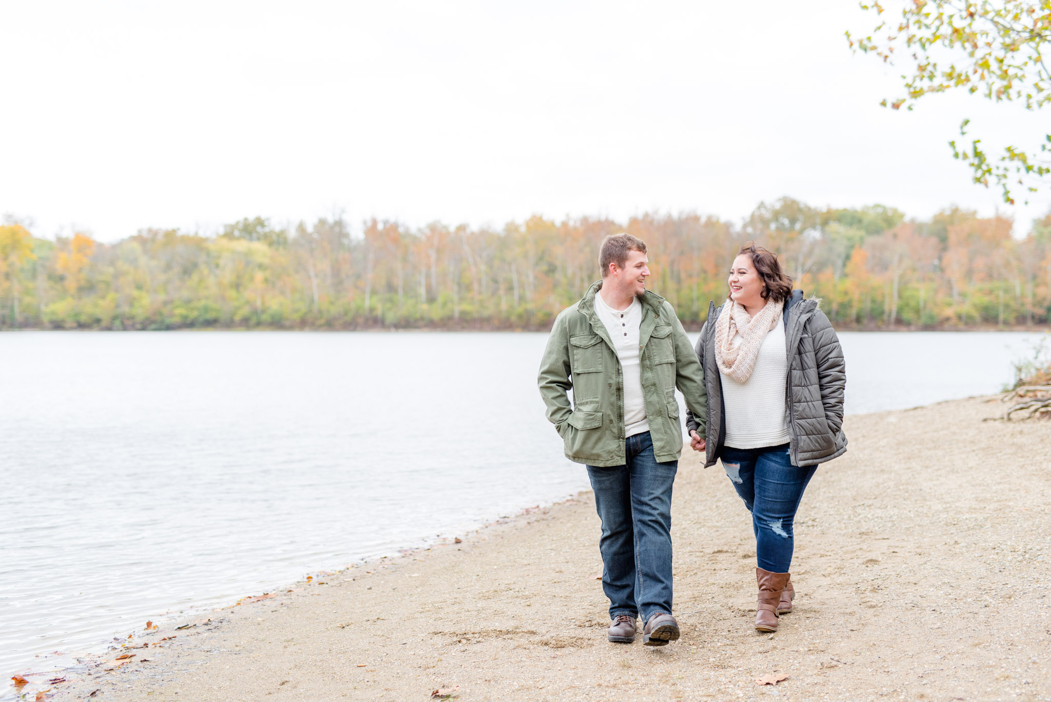 Bride and groom walk along riverbank during engagement pictures.