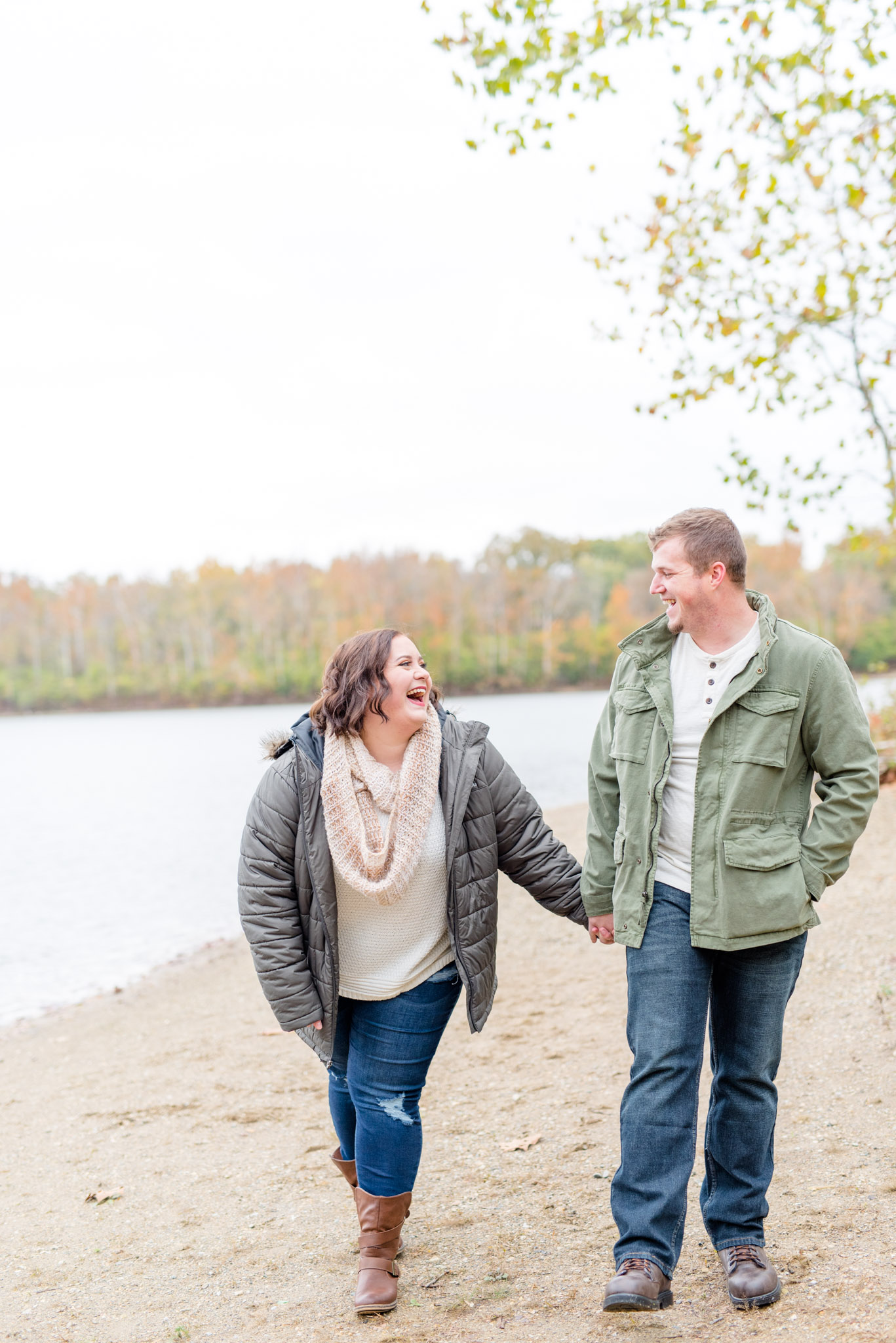 Engaged couple laughs while walking along riverbank.