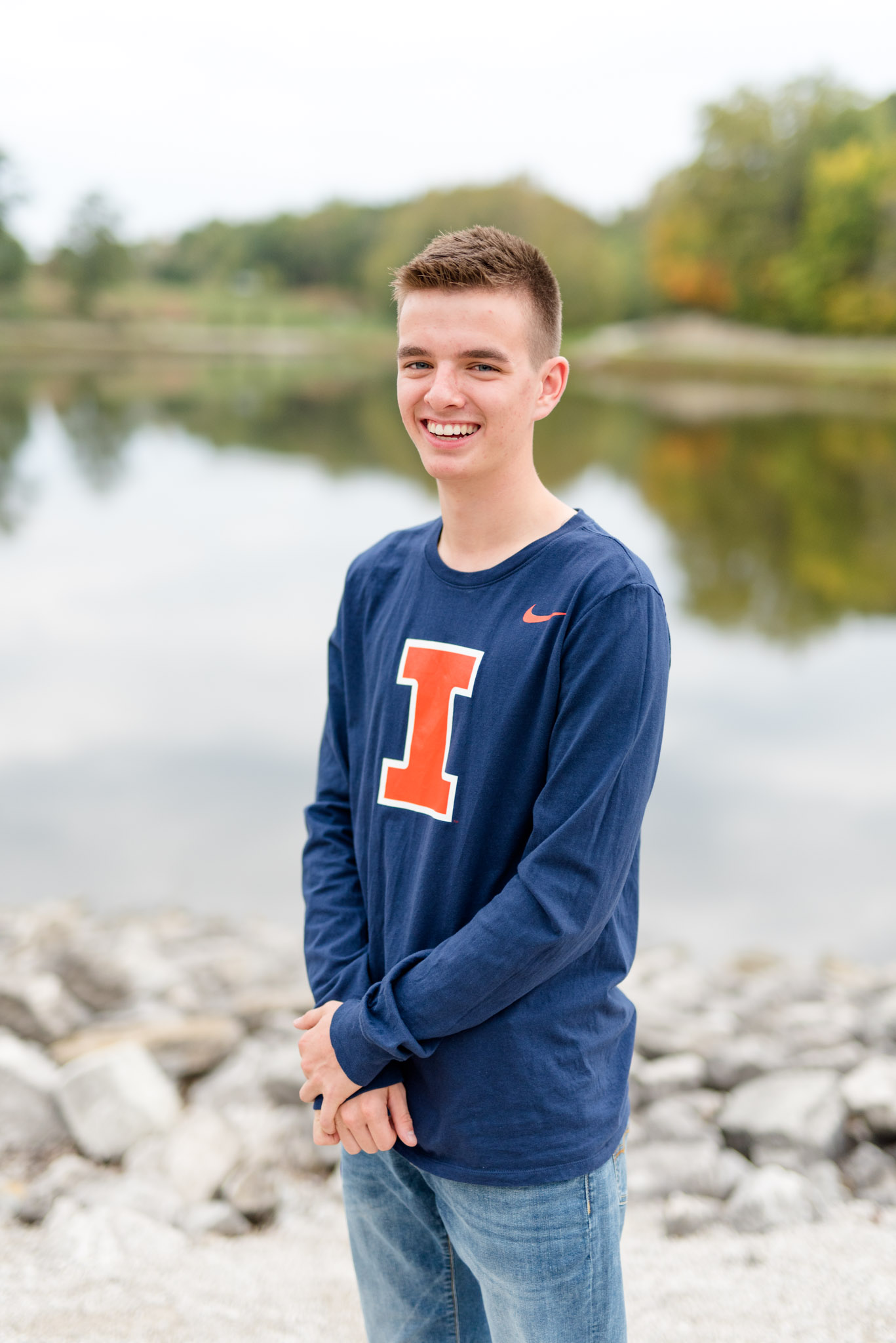Senior guy stands in front of lake during fall.