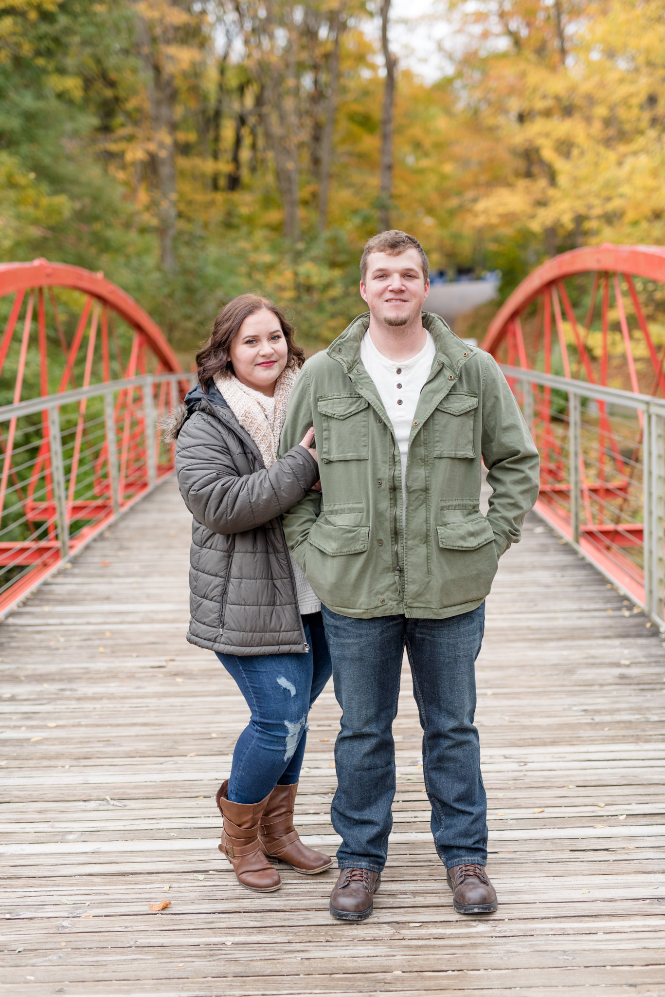 Engaged couple stands on red bridge.