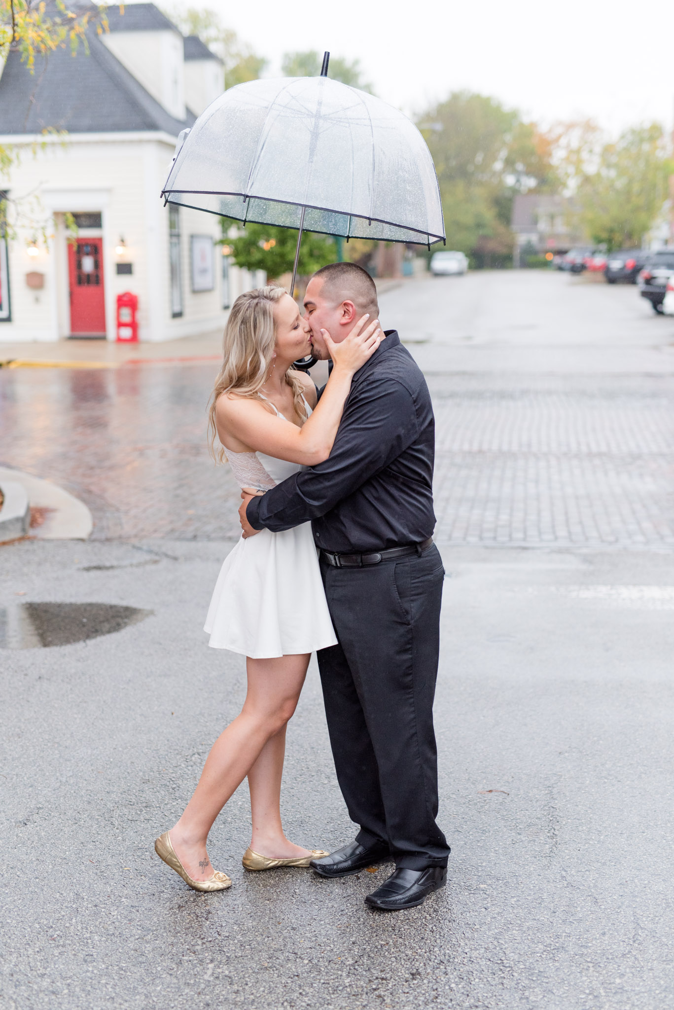 Bride and groom kiss under umbrella on downtown street.