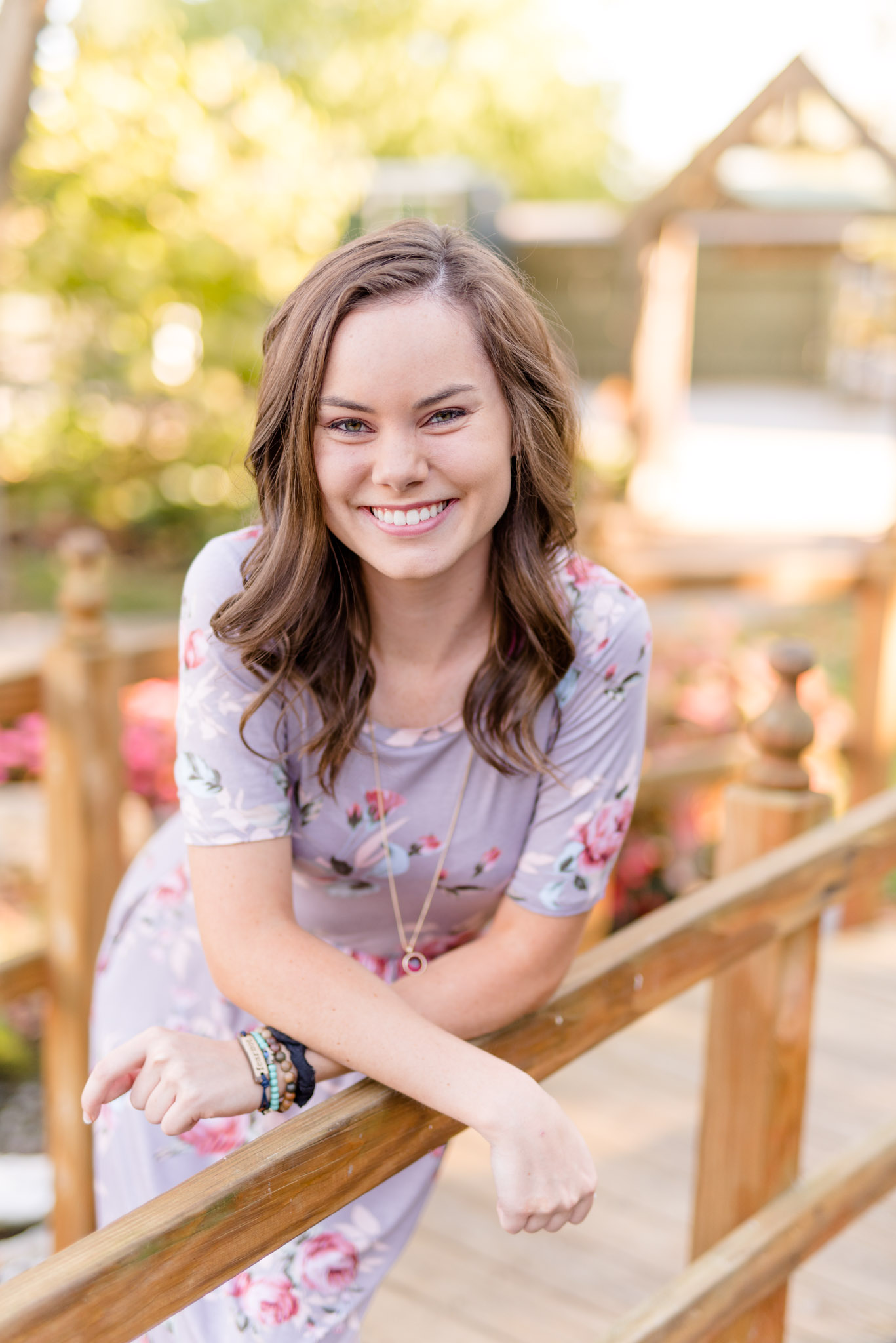 Senior girl leans over bridge railing and smiles.