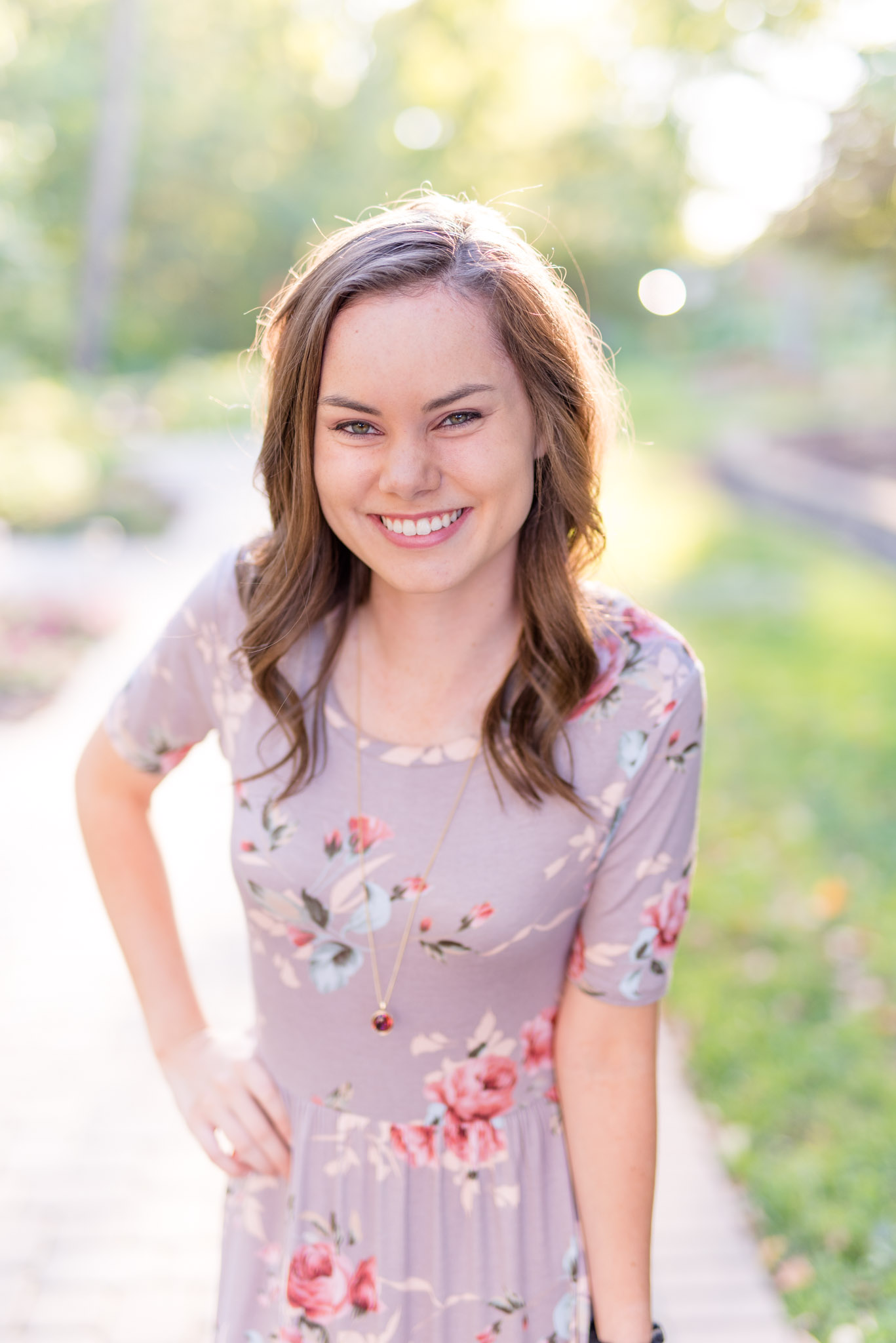 Senior girl smiles while standing on garden path.