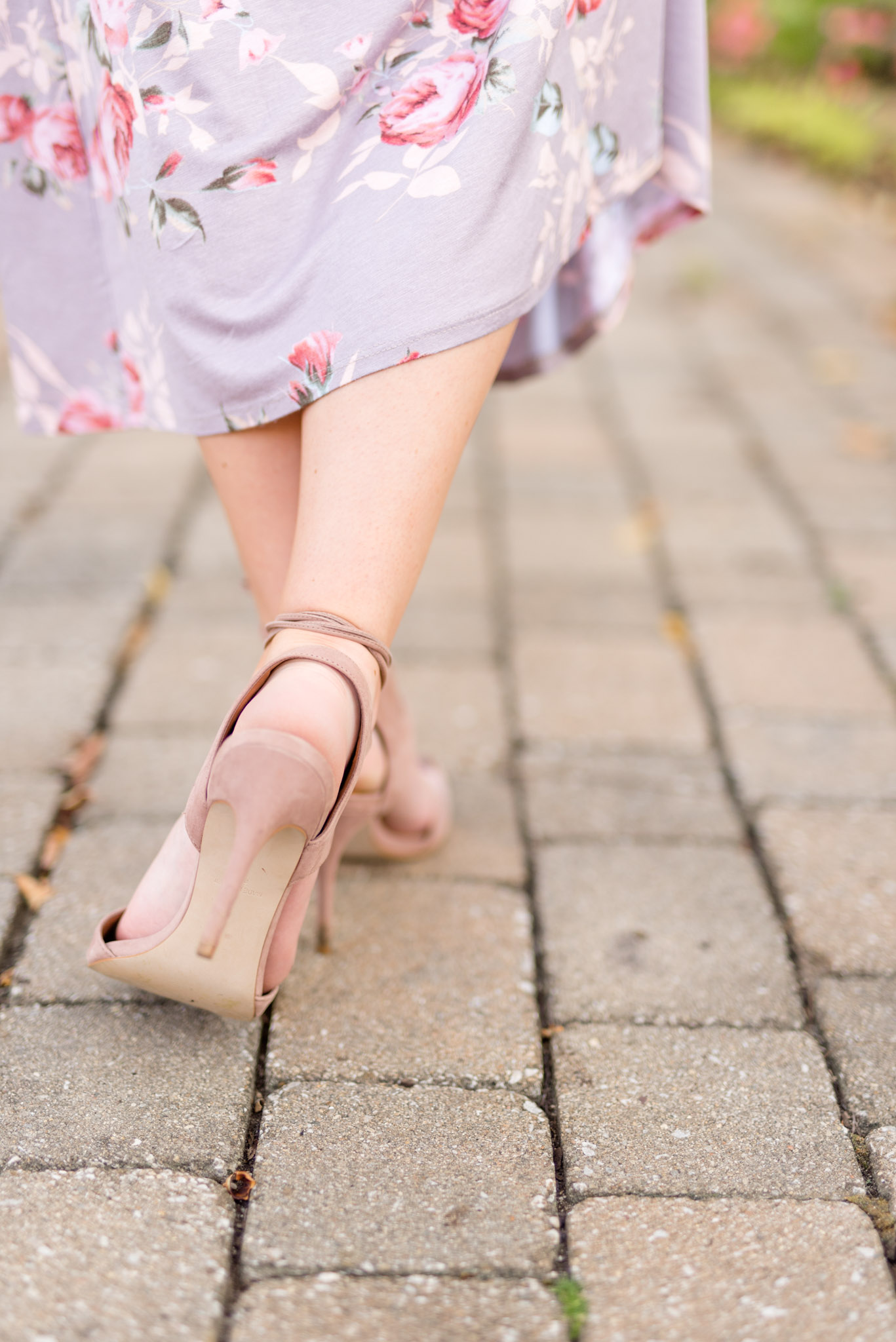 Girl wearing high heels walks along brick path.