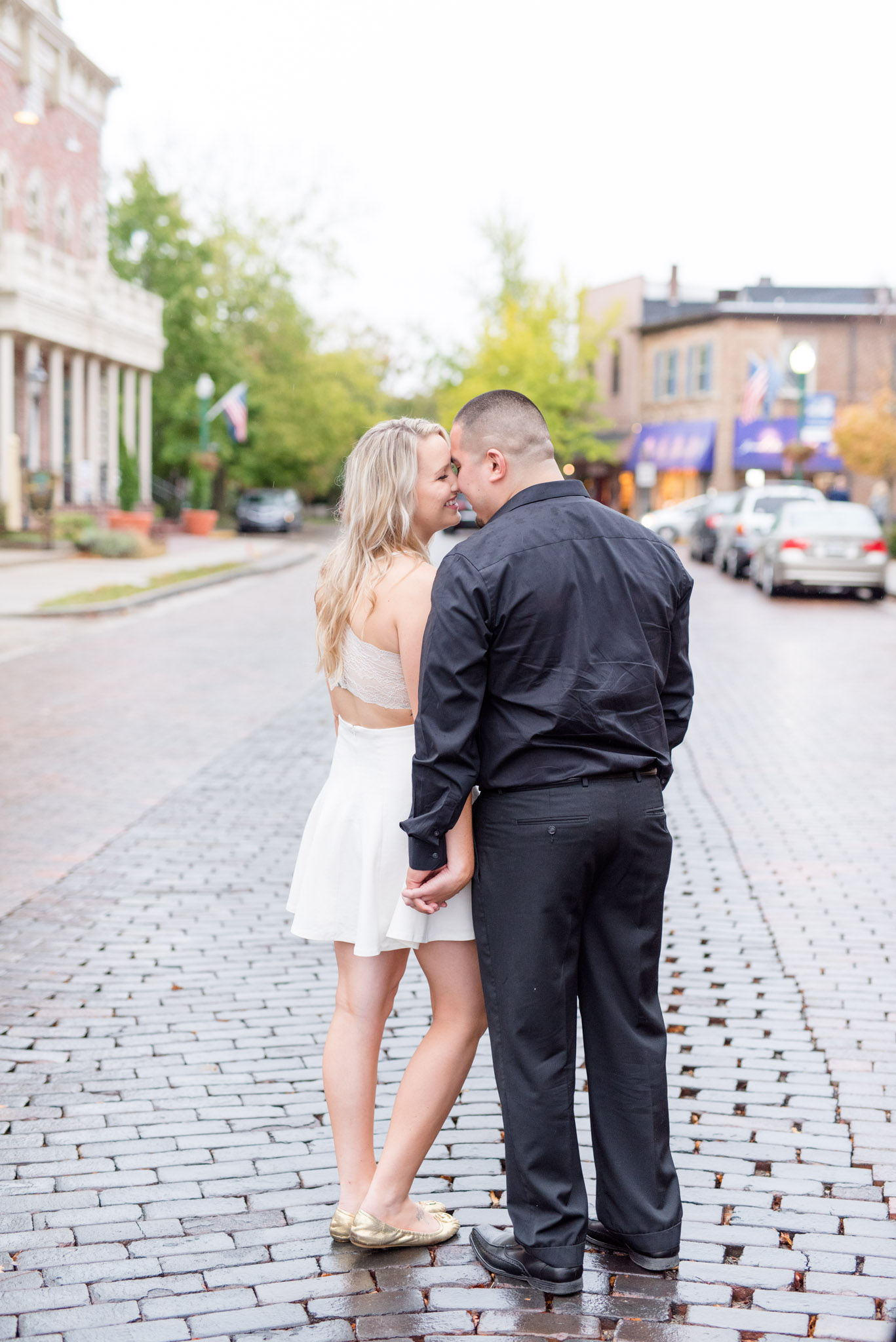 Engaged couple face away from camera on downtown street.