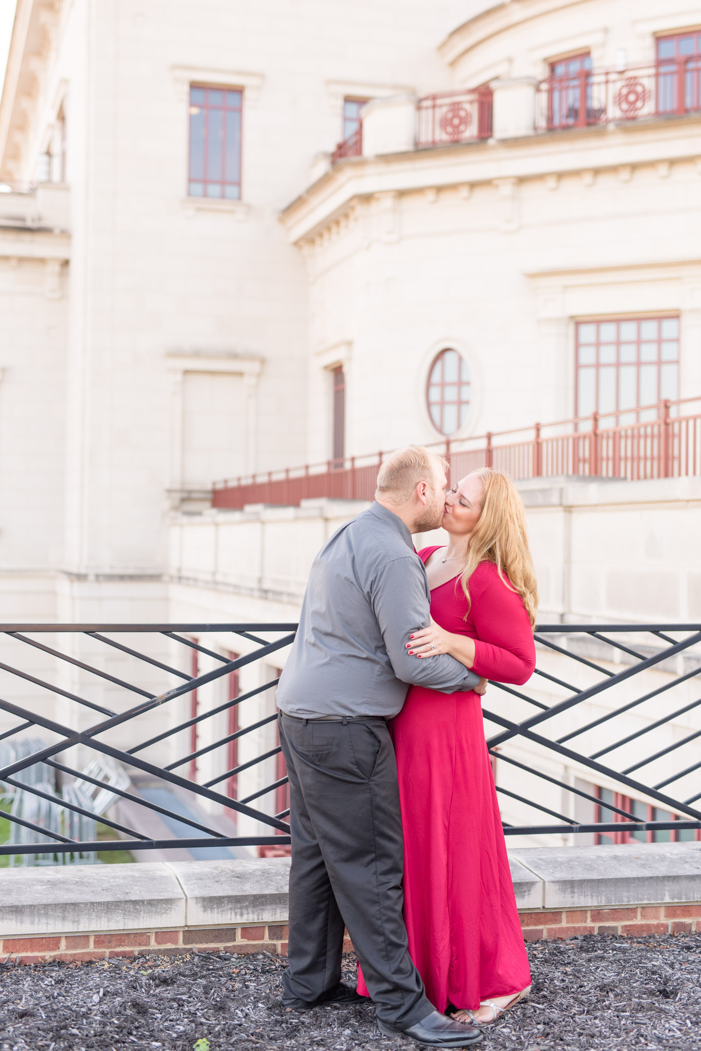 Engaged Couple Kissing in front of large white building