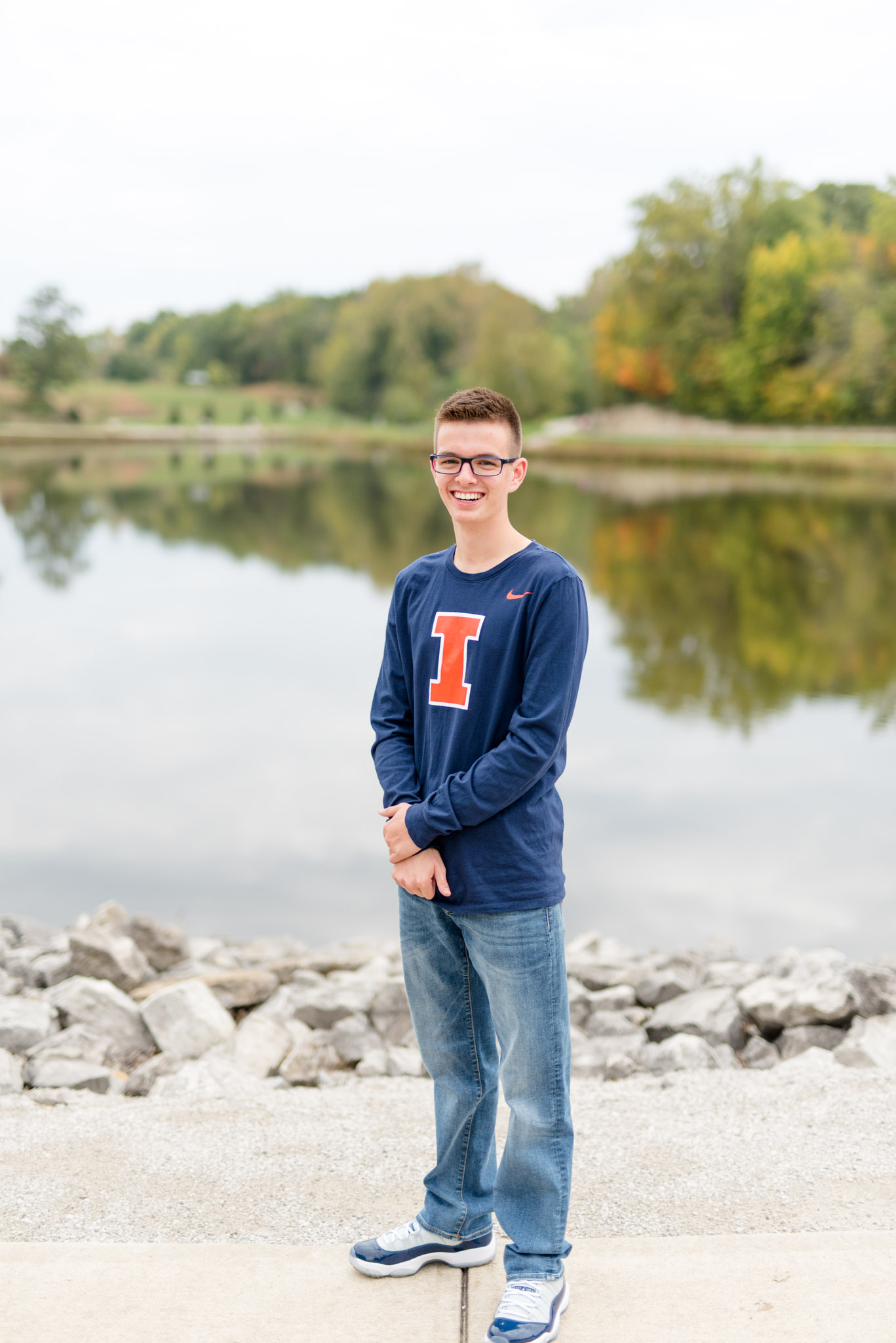 Senior guy stands in front of lake during fall.