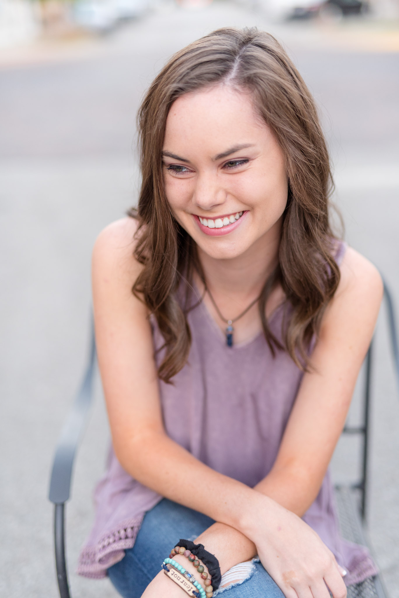 Senior girl sits in chair and smiles off camera.
